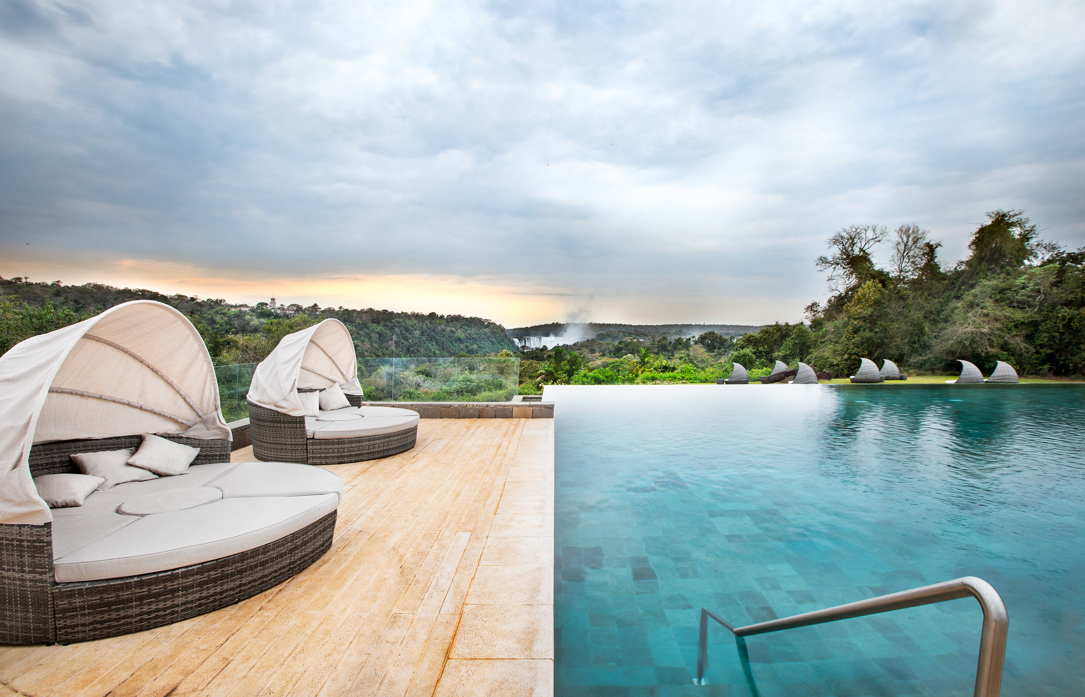 Luxury infinity pool with sun loungers overlooking Iguazu Falls and lush forest.