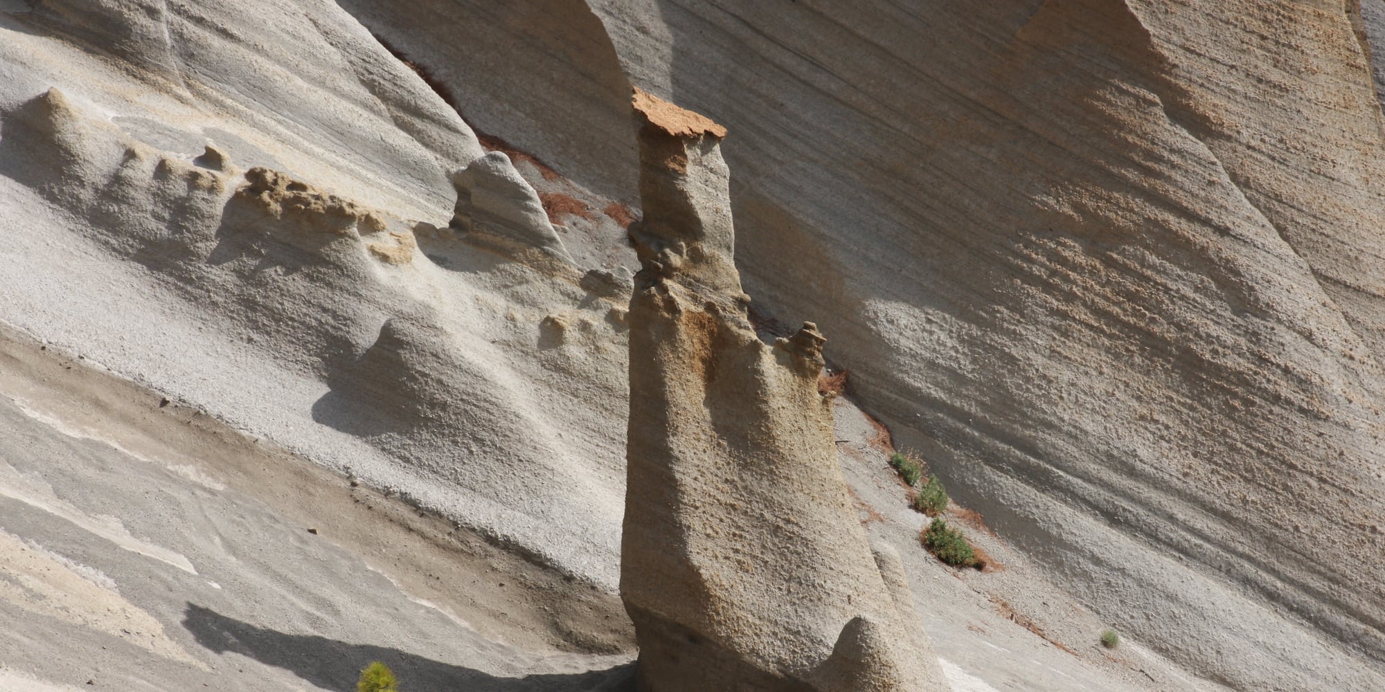 Eroded rock hoodoo against layered volcanic ash formations.