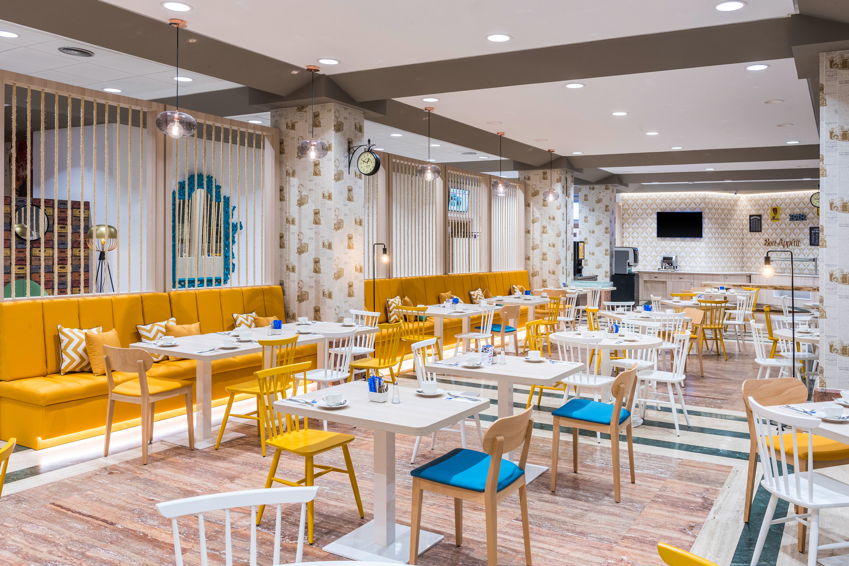 Modern restaurant dining room with vibrant yellow booths and diverse chairs.