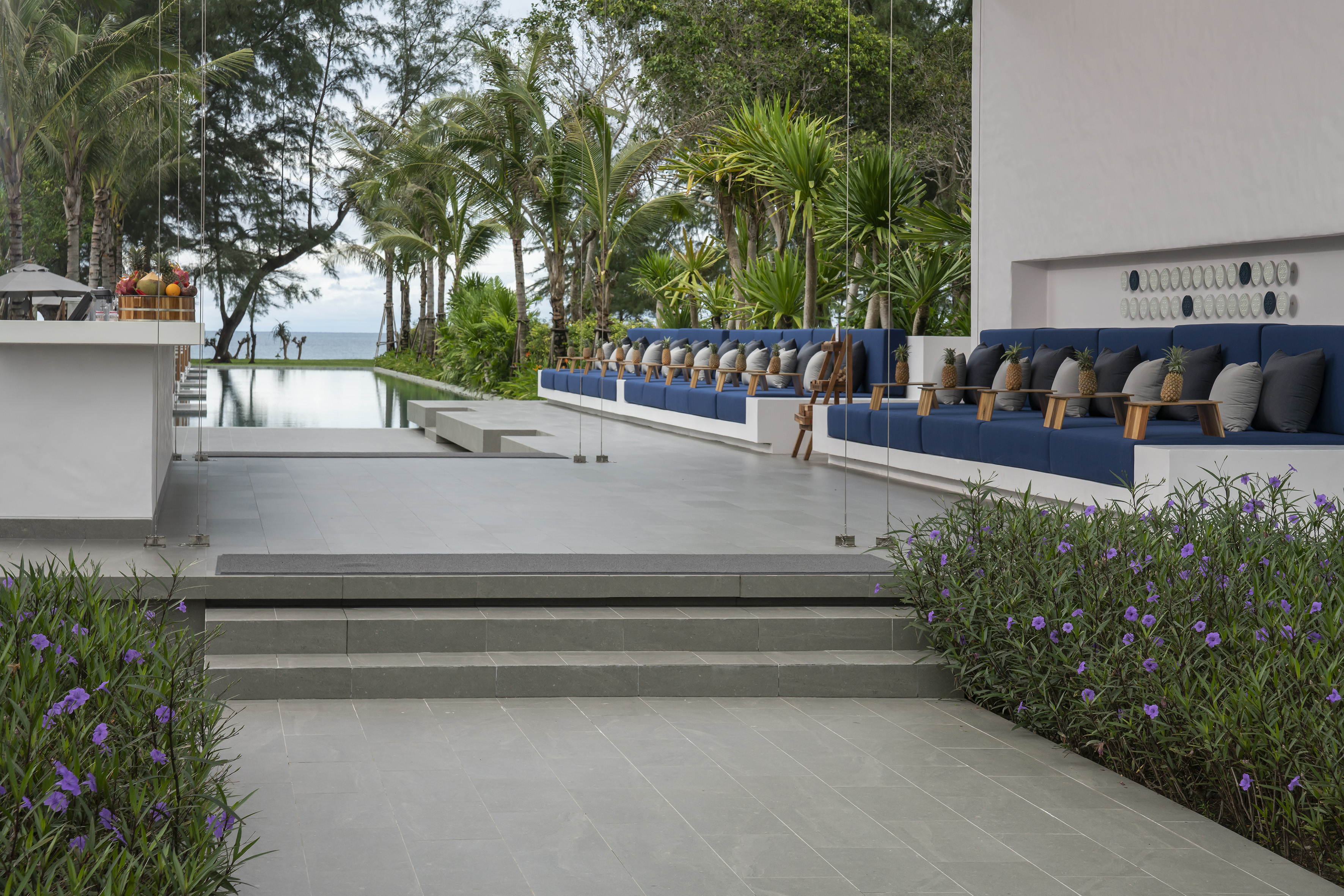 Tropical resort lounge with infinity pool, ocean view, and lush palm trees.