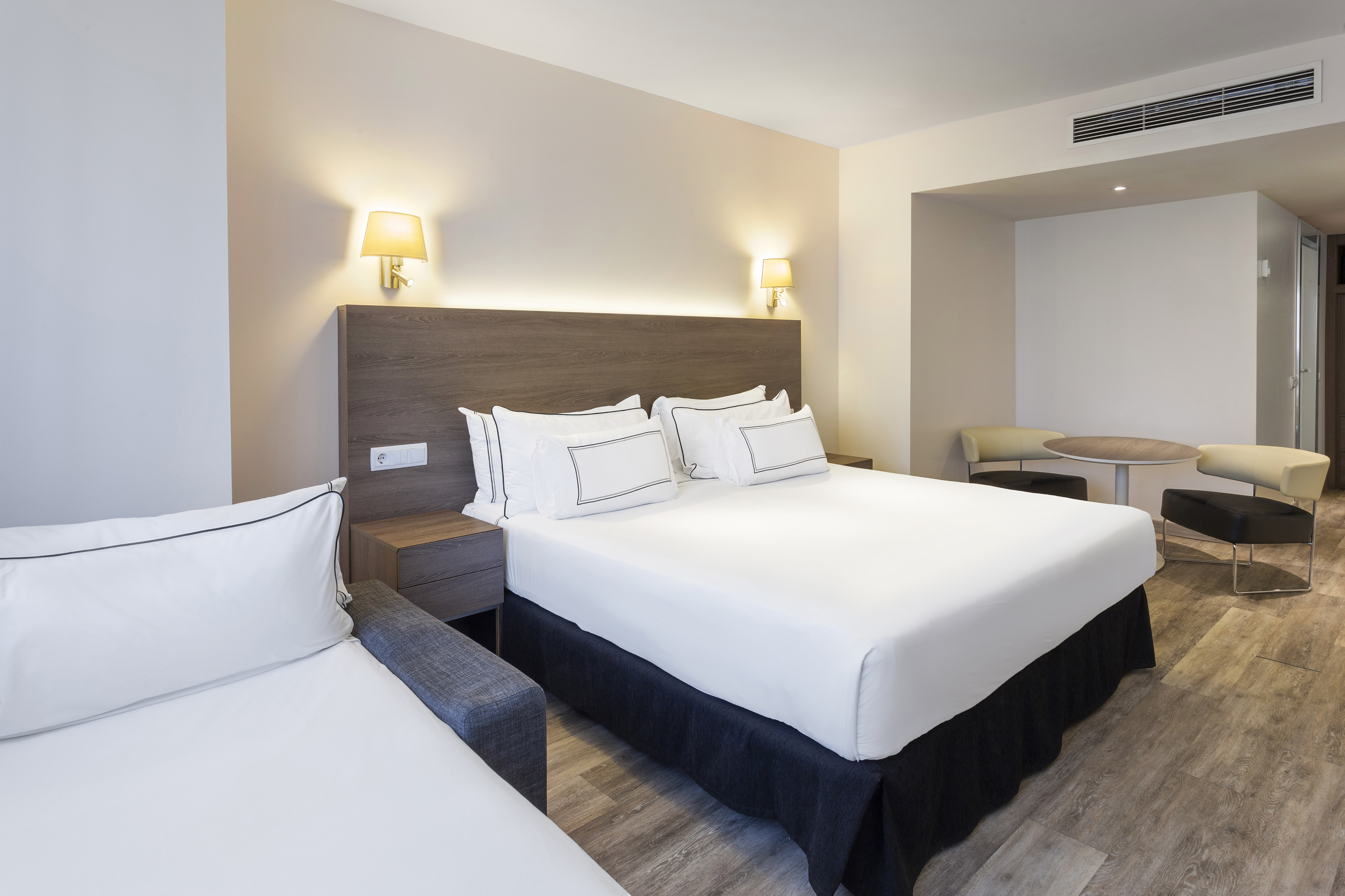 Modern hotel suite with king bed, sofa bed, and seating area.