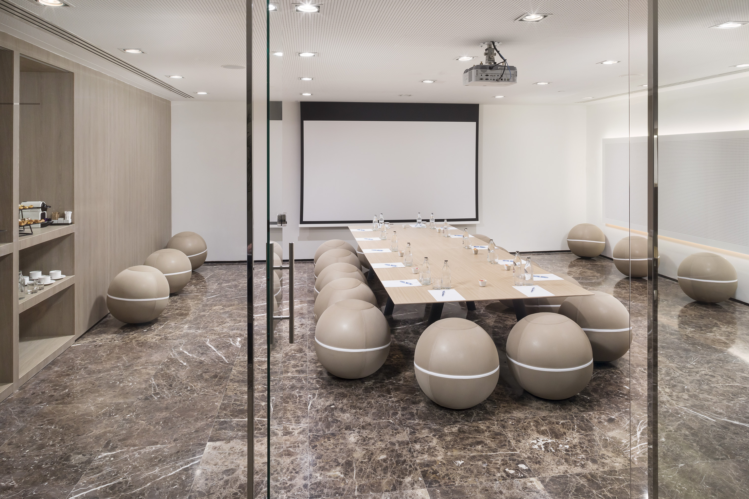 Modern conference room with spherical chairs, wooden table, projector, marble floor.
