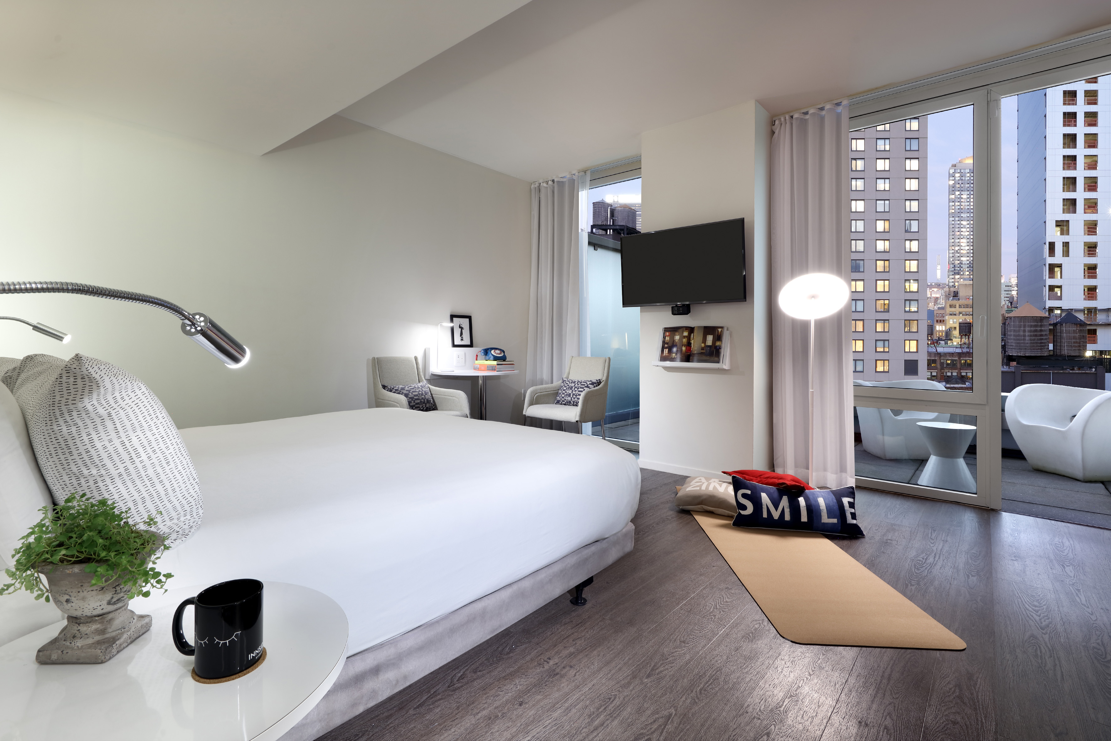 Modern hotel room with large bed, city view balcony, and yoga mat.
