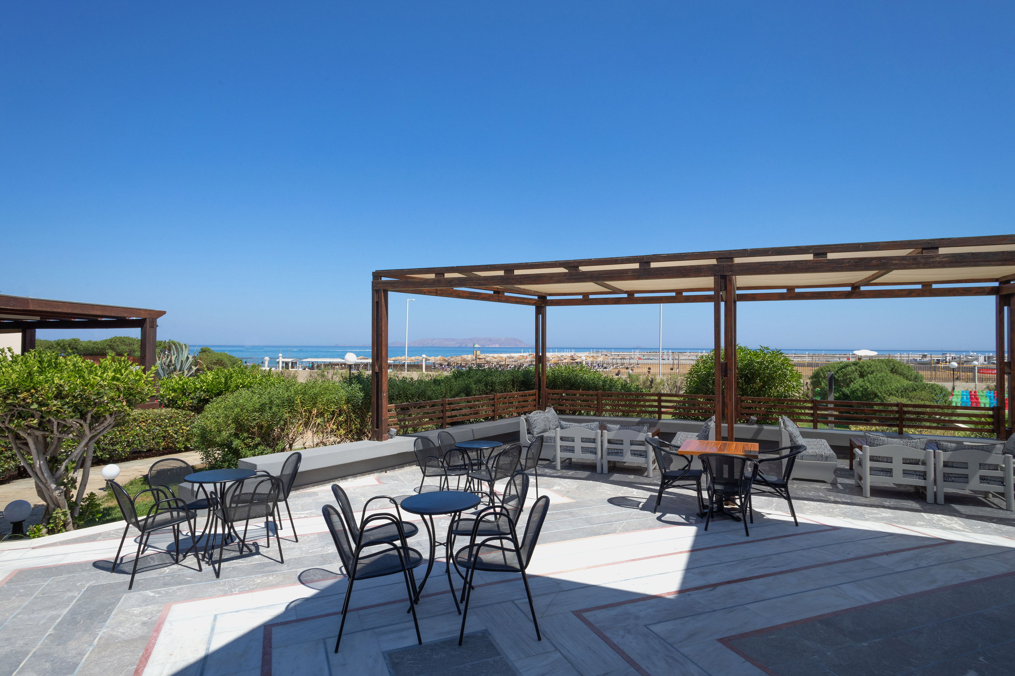 Outdoor resort patio with cafe tables, shade pergola, and ocean view beach.