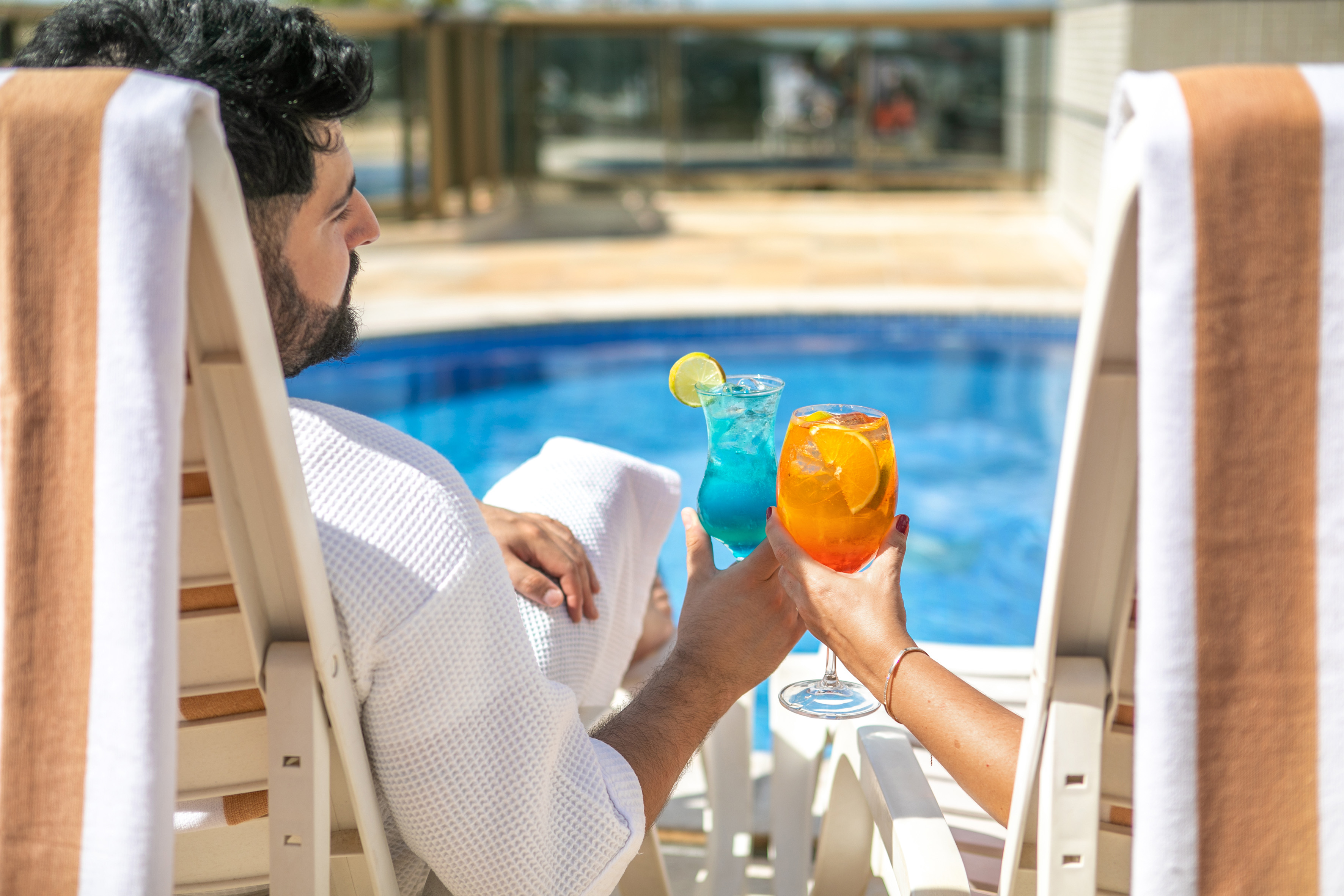 Couple relaxing by pool with colorful cocktails at a resort.