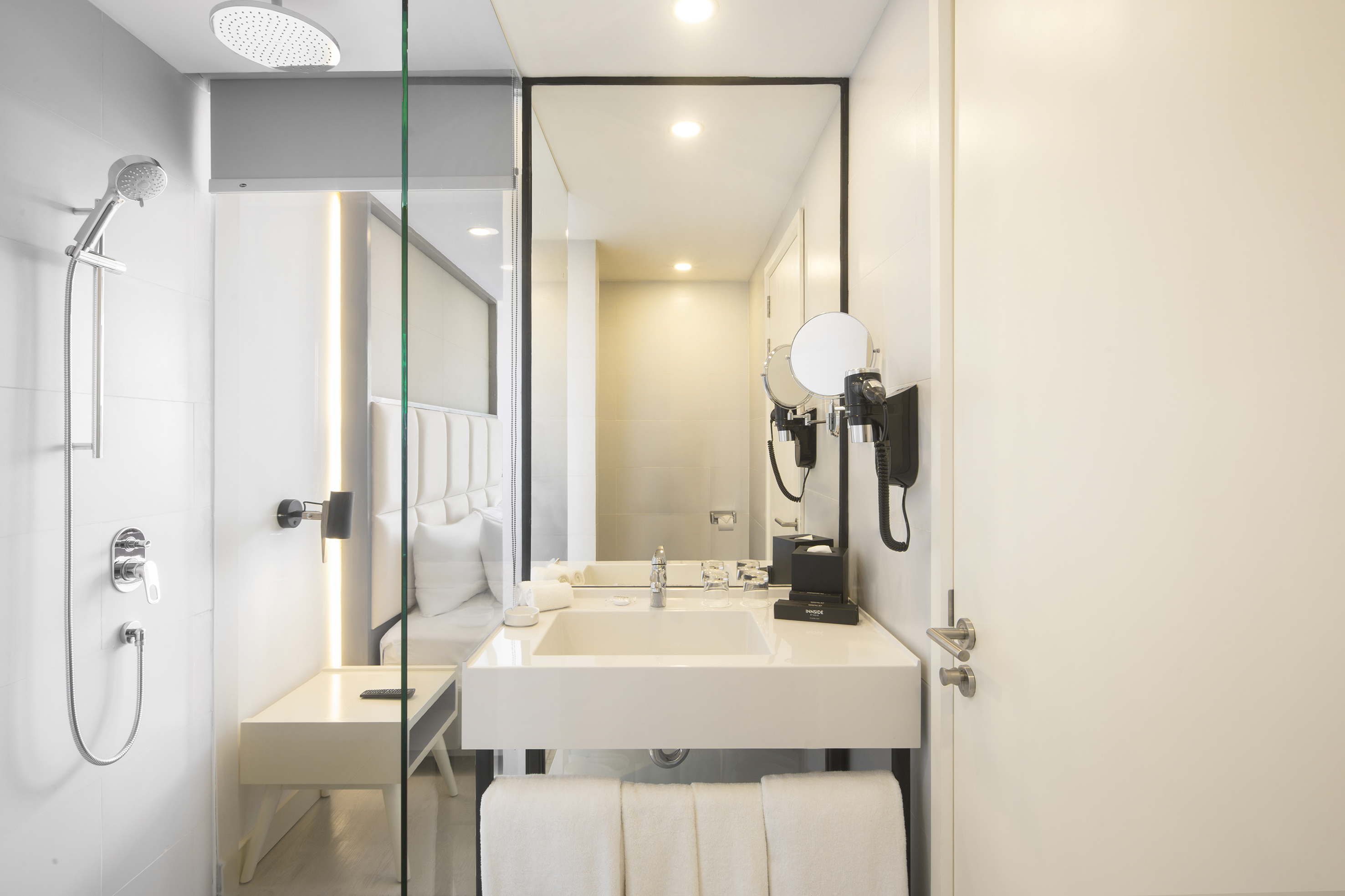 Modern white hotel bathroom with vanity, sink, large mirror, and glass shower.