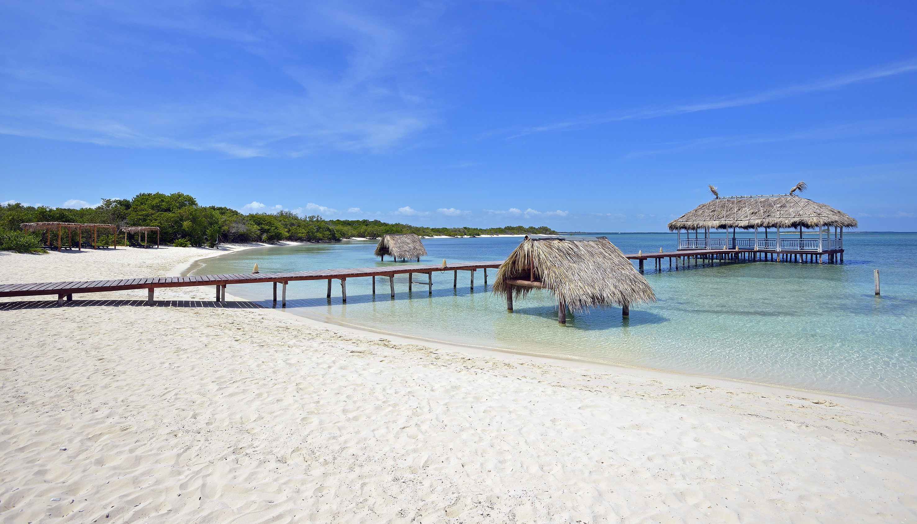 a dock over water with straw huts and a beach