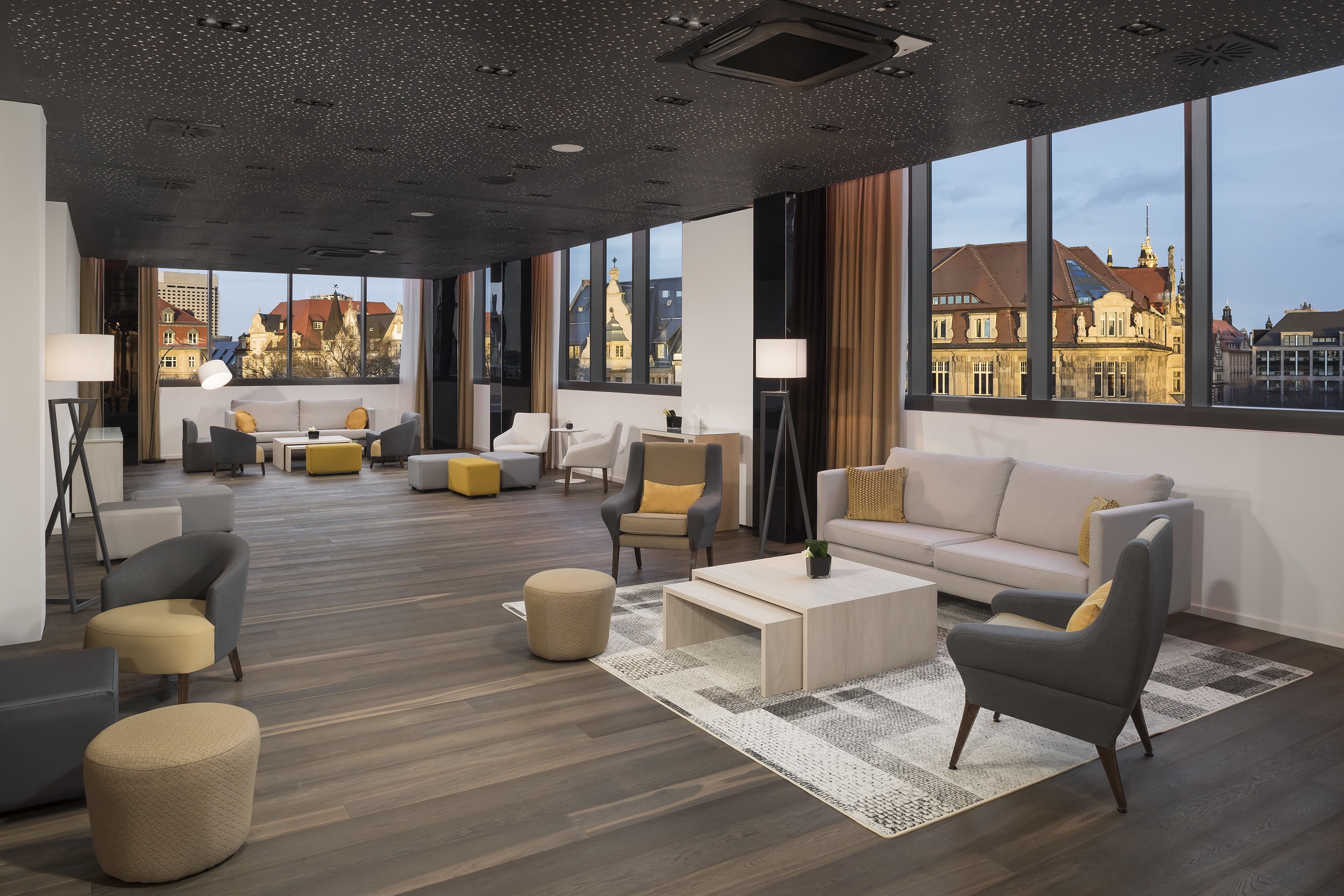 Modern hotel lounge with city view, grey and yellow contemporary seating.