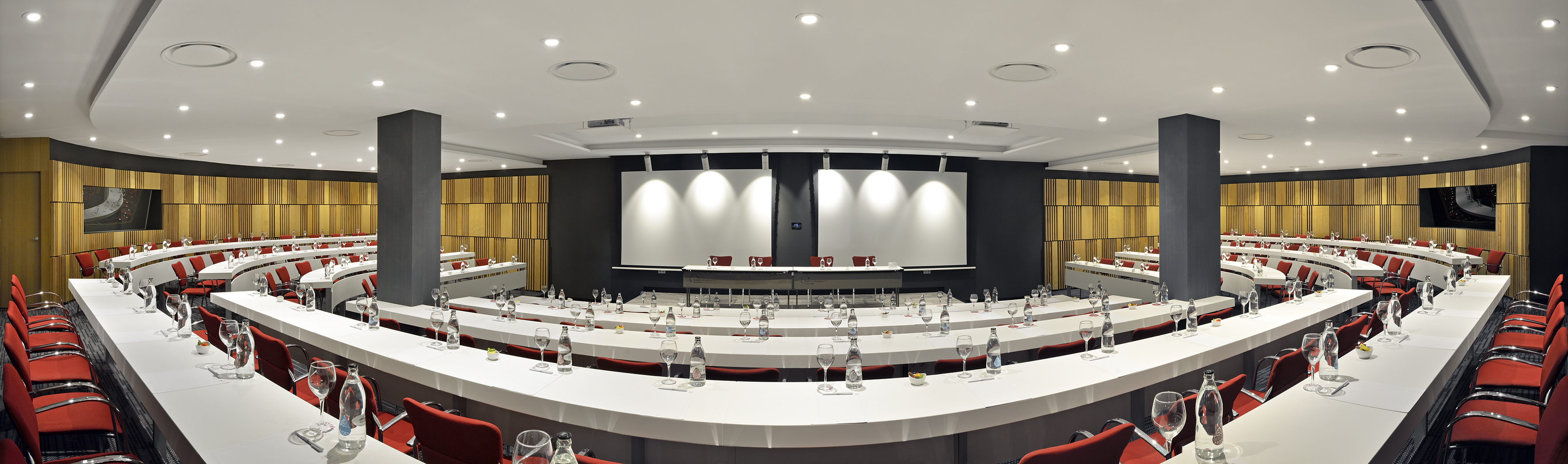 Modern conference room with curved white tables, red chairs, and dual projection screens.