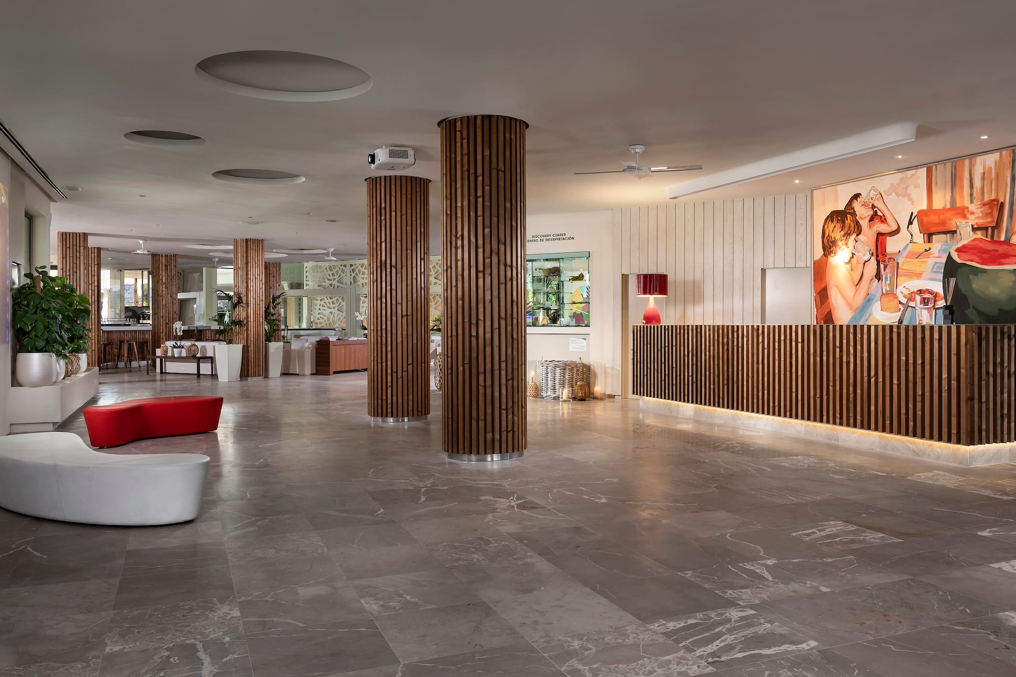 Modern hotel reception with wooden desk, large artwork, and lounge seating.