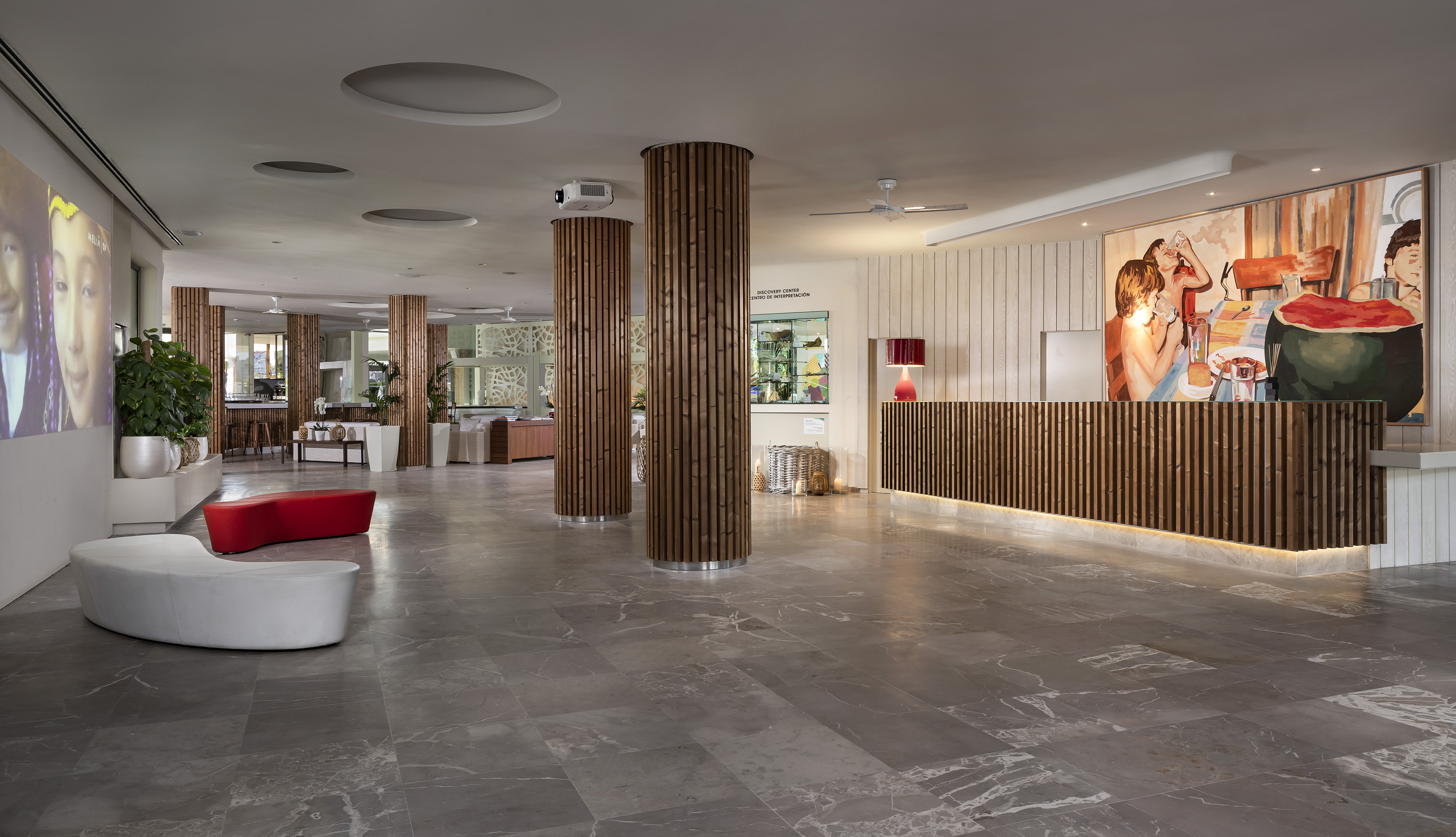 Modern hotel reception with wooden desk, large artwork, and lounge seating.