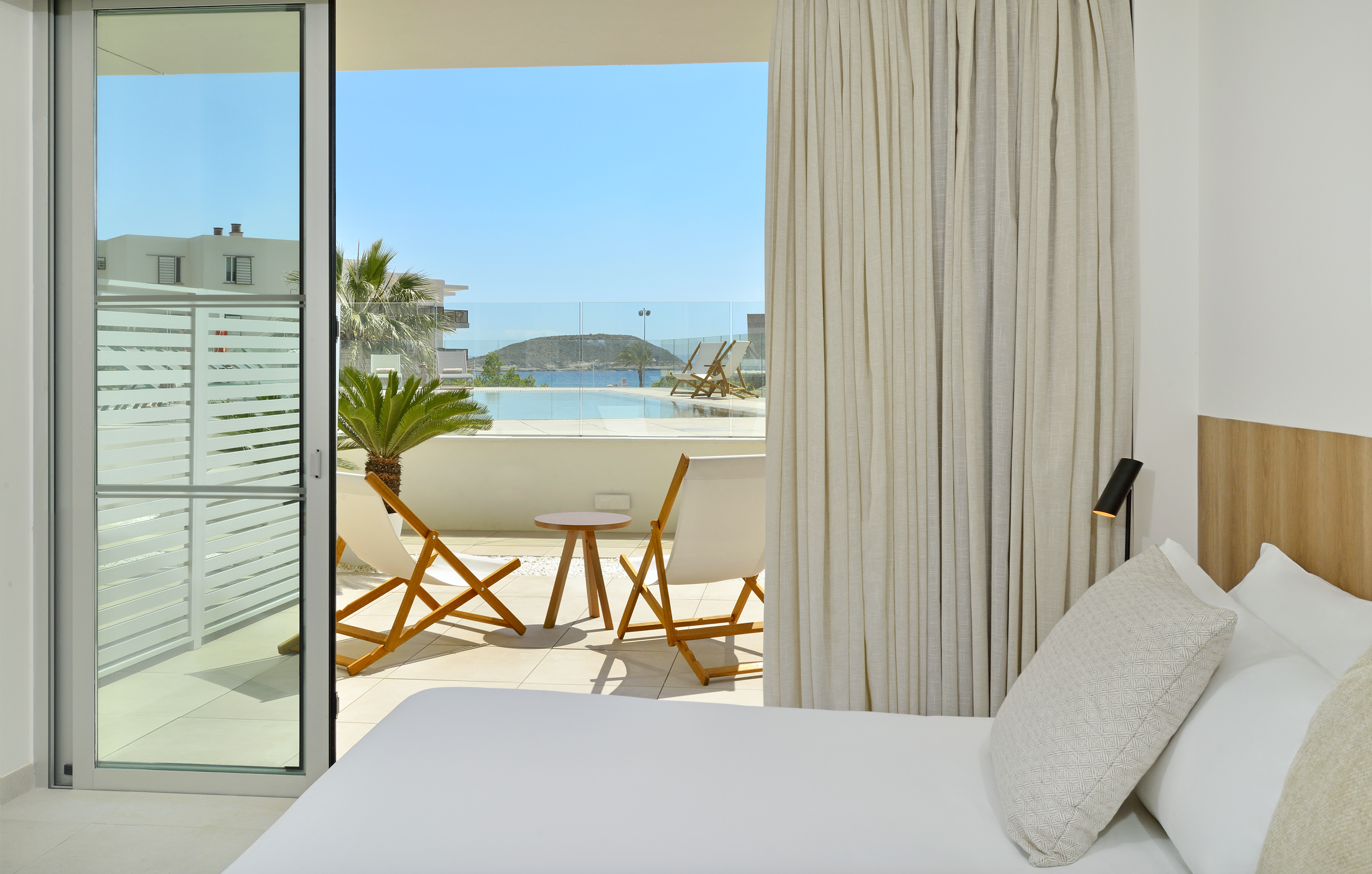 Modern hotel room with private pool balcony, sun loungers, and sea view.