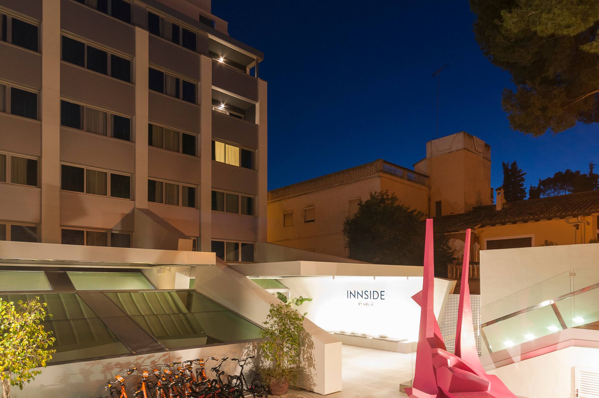 INNSiDE hotel night exterior with illuminated sign, modern courtyard, pink sculpture, bikes.