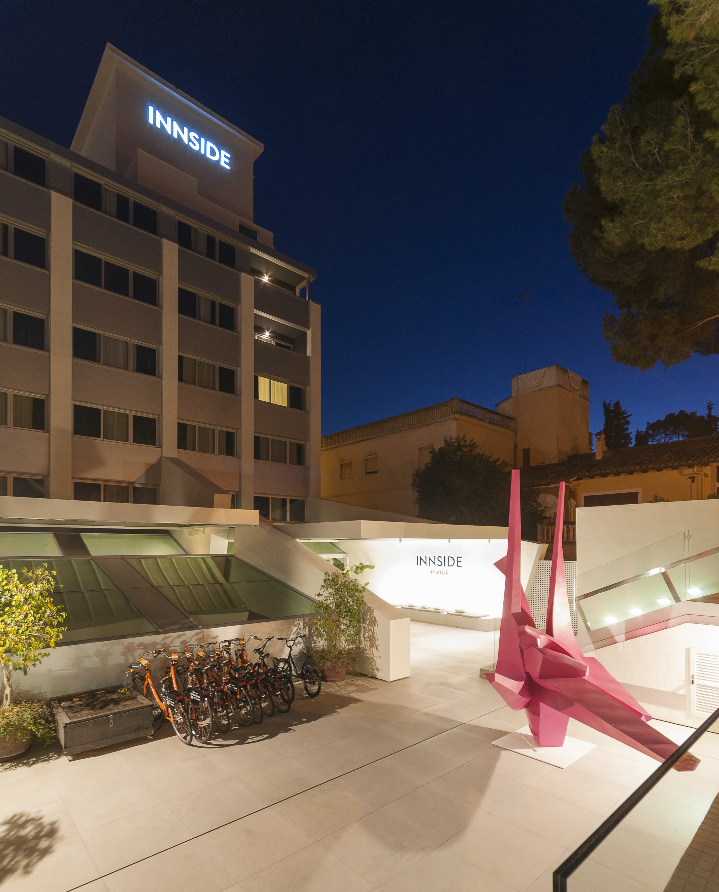 INNSiDE hotel night exterior with illuminated sign, modern courtyard, pink sculpture, bikes.