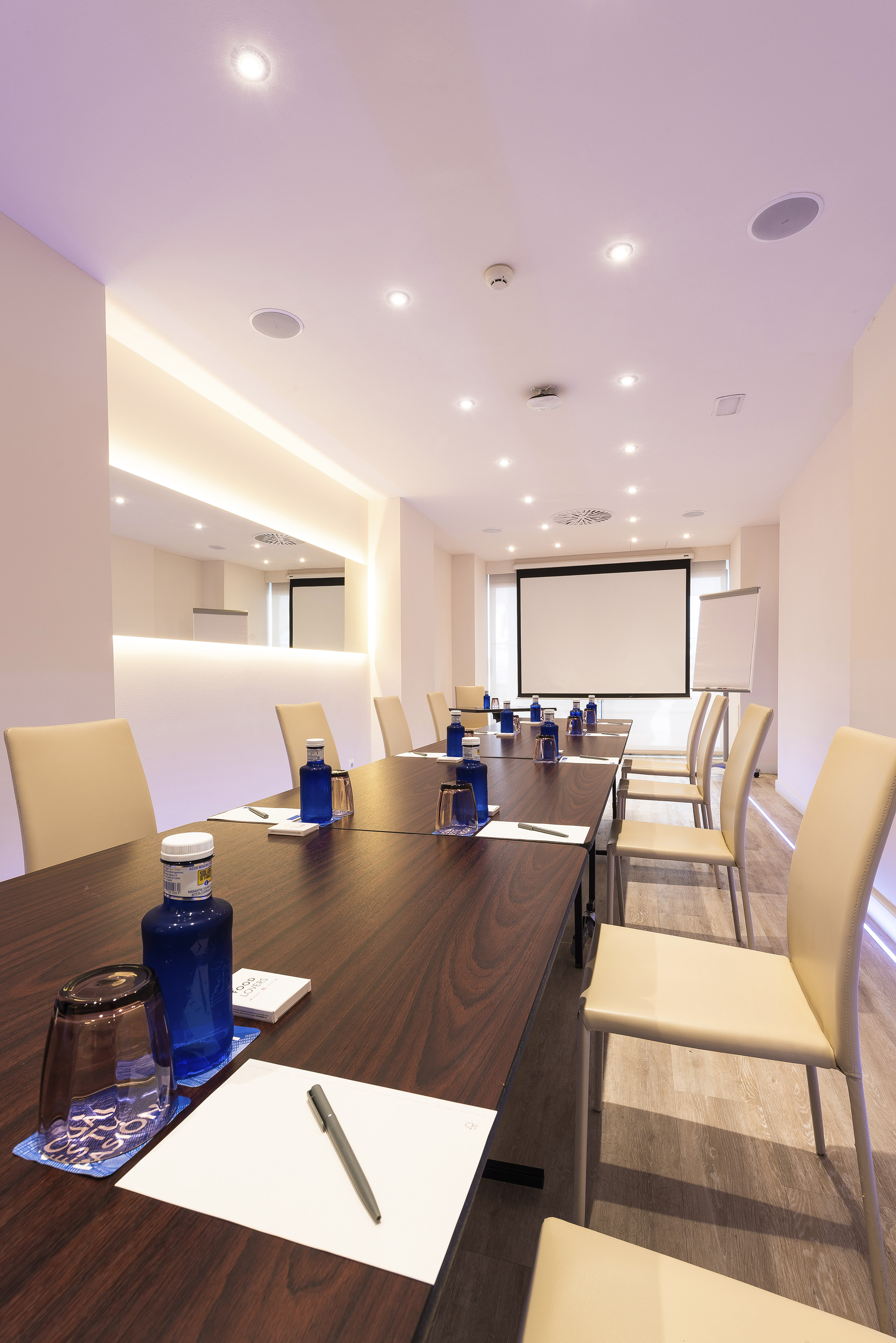 Modern conference room with long table, projector screen, and water bottles.