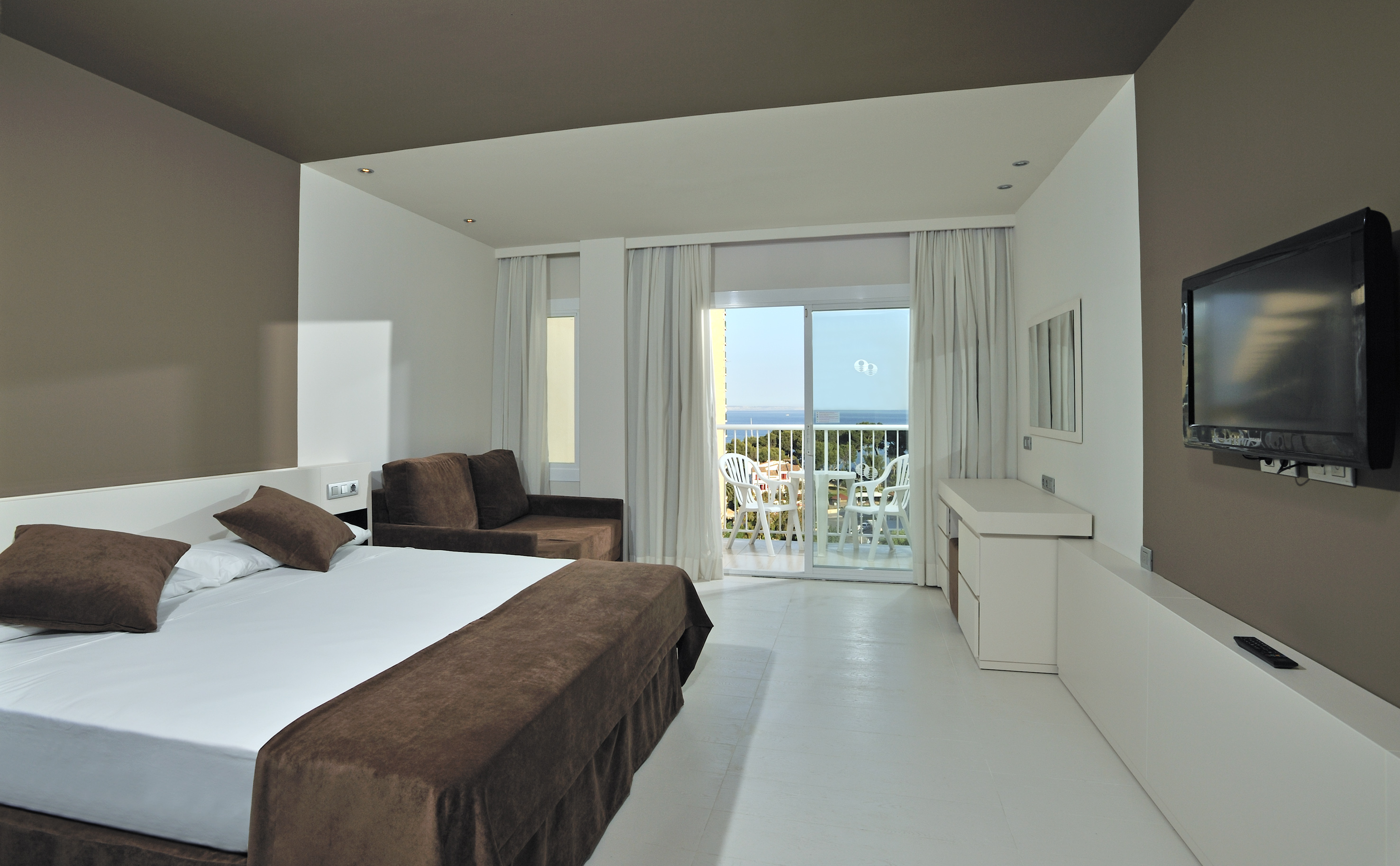 Modern hotel room with sea view balcony, white bed, and brown sofa.