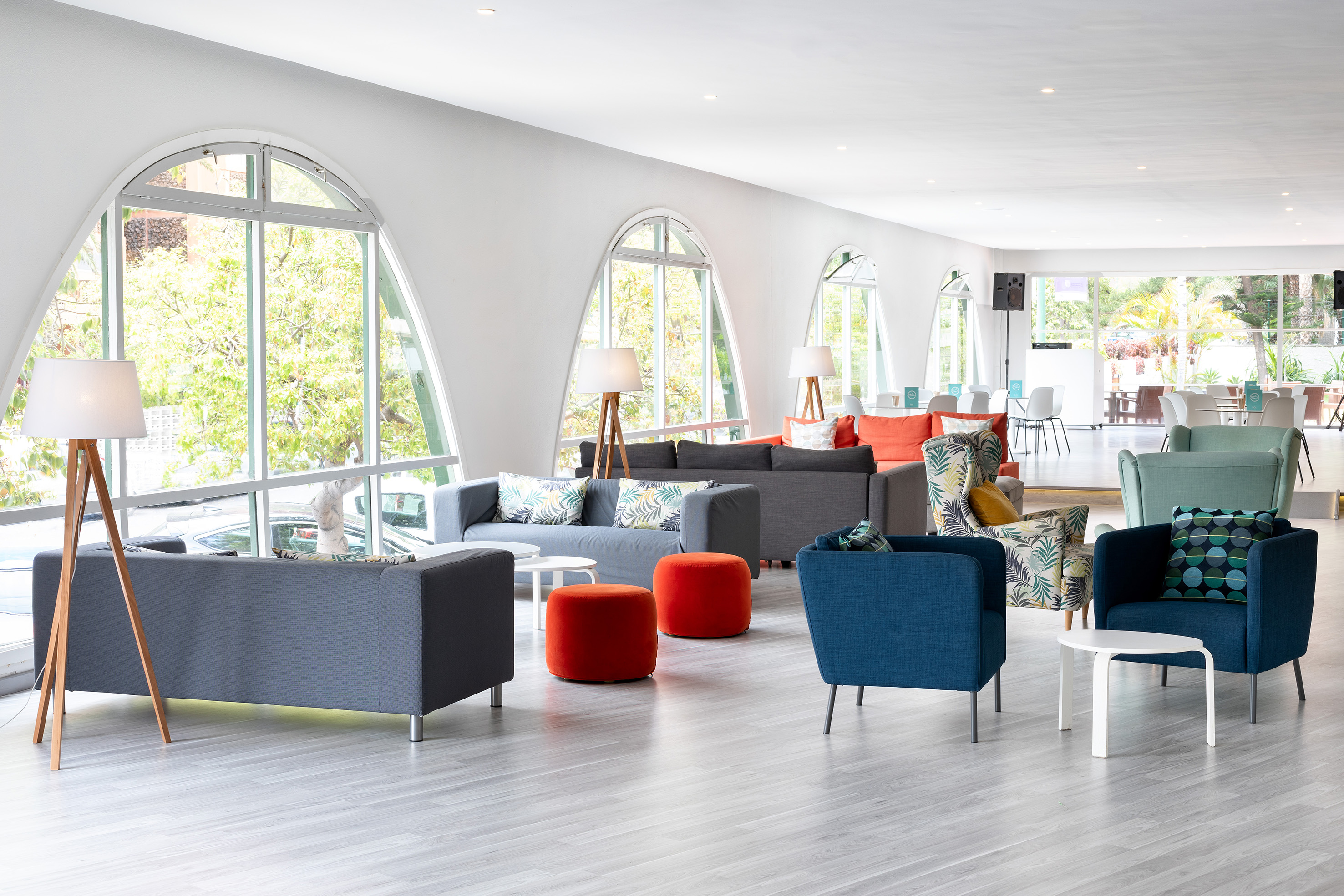 Bright modern hotel lounge with colorful sofas, armchairs, and large arched windows.