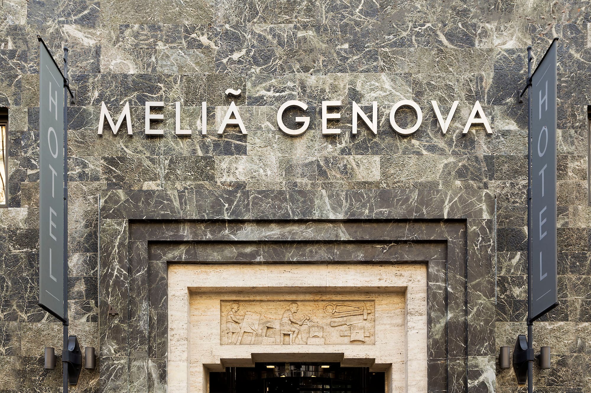 Melia Genova hotel sign on dark marble facade, with carved entrance.