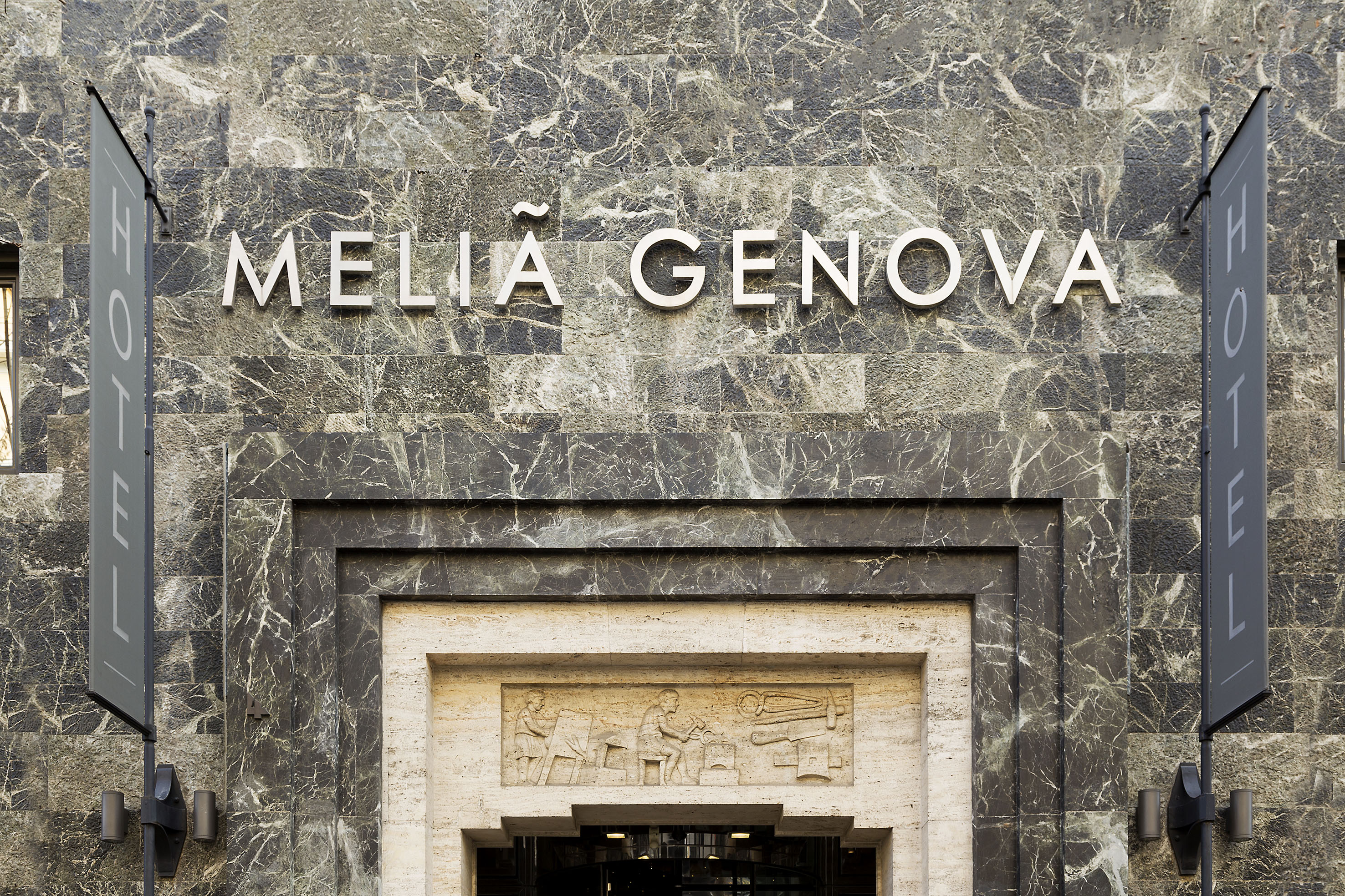 Melia Genova hotel sign on dark marble facade, with carved entrance.