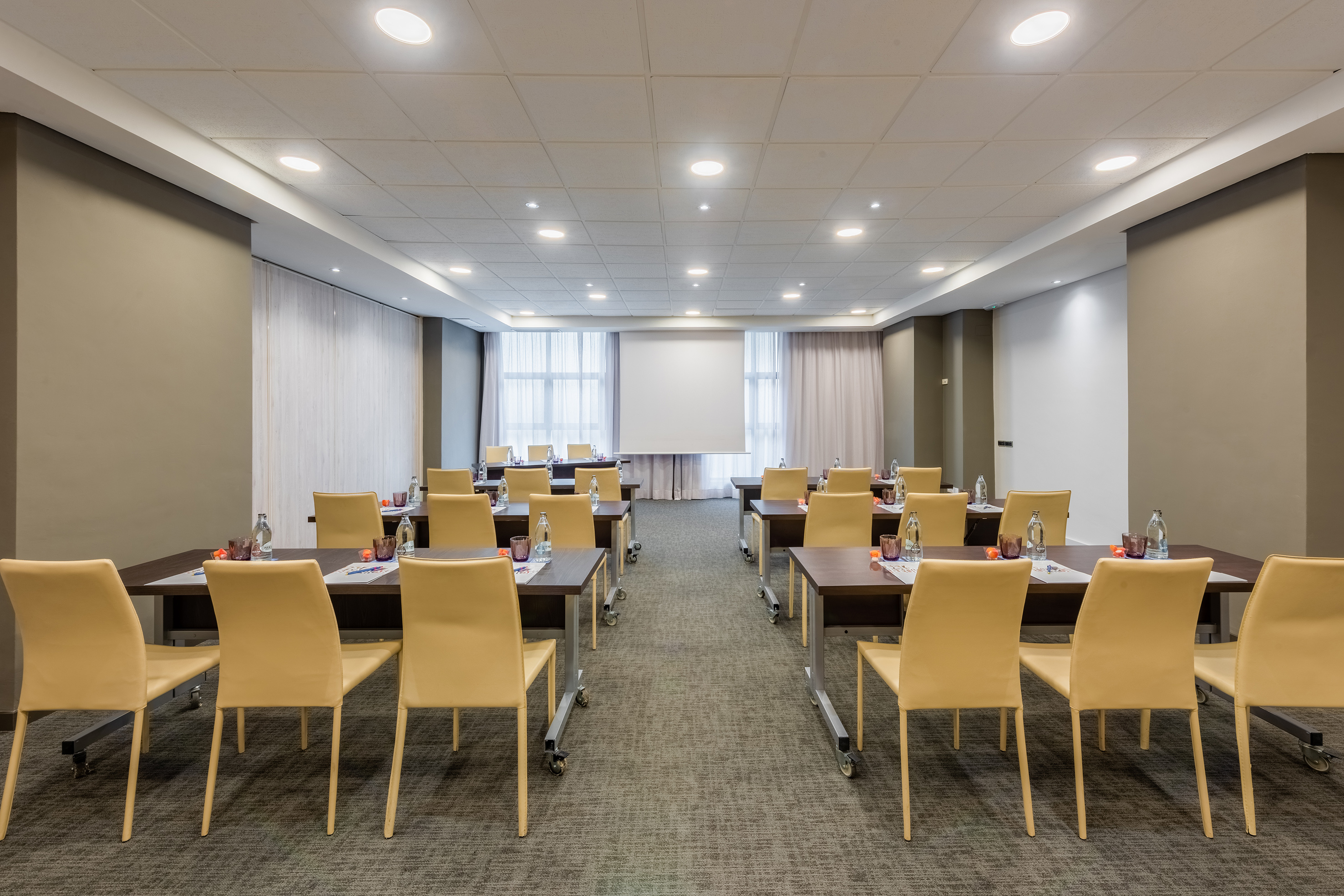 Professional conference room with tables, beige chairs, and presentation screen.