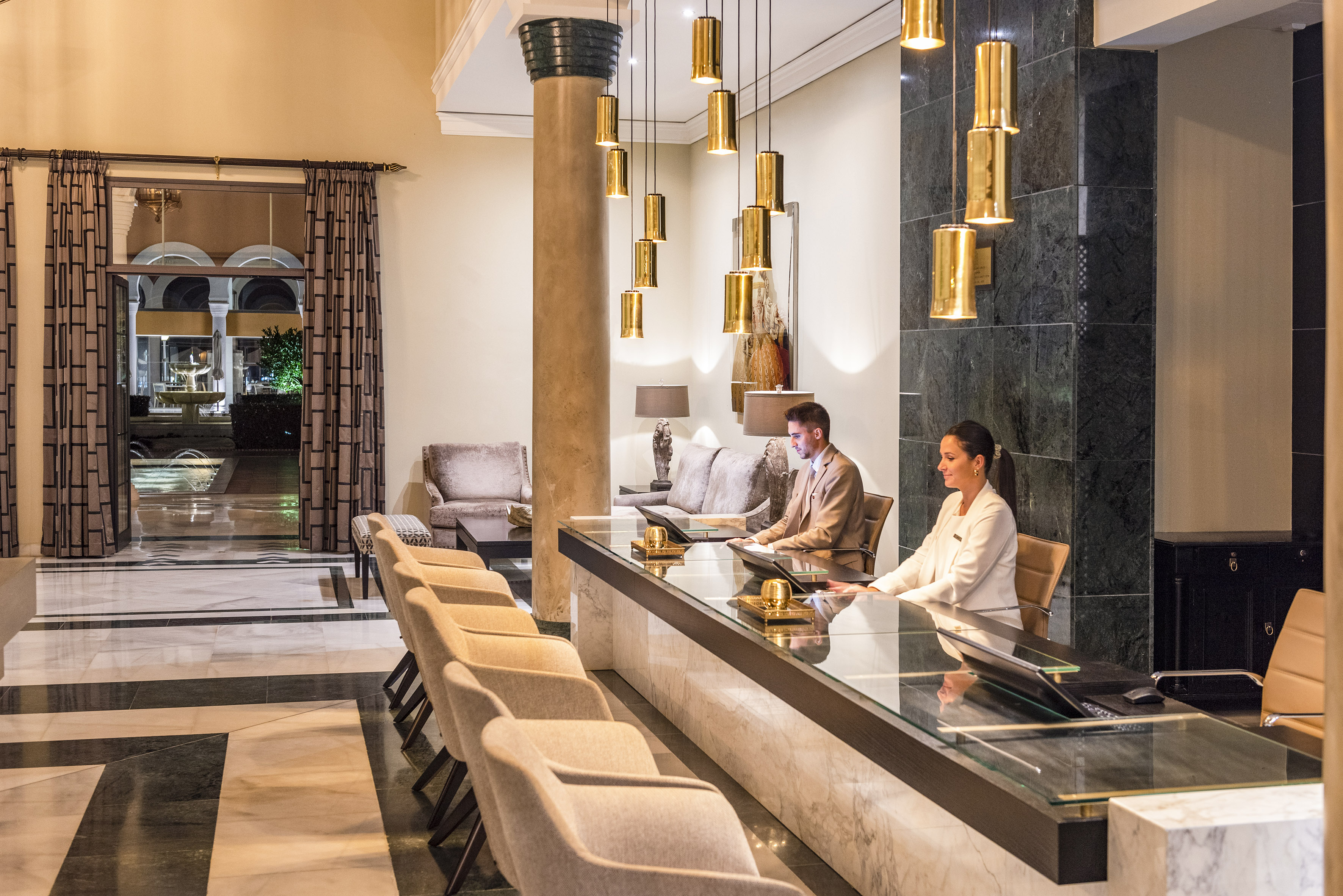 Elegant hotel reception with staff at front desk, gold lights, marble interior.