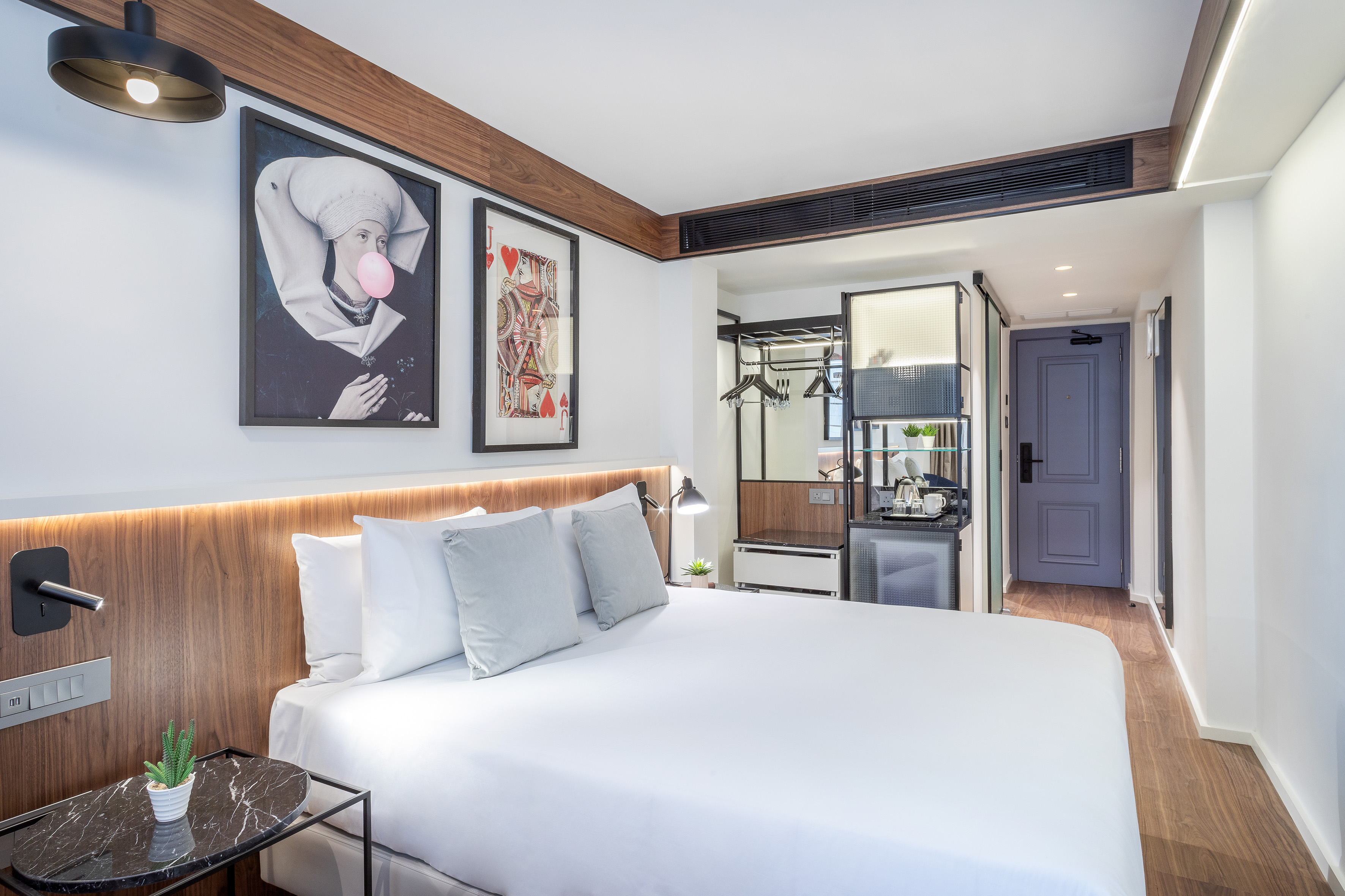 Modern hotel room with queen bed, wooden headboard, unique art, and mini-bar.