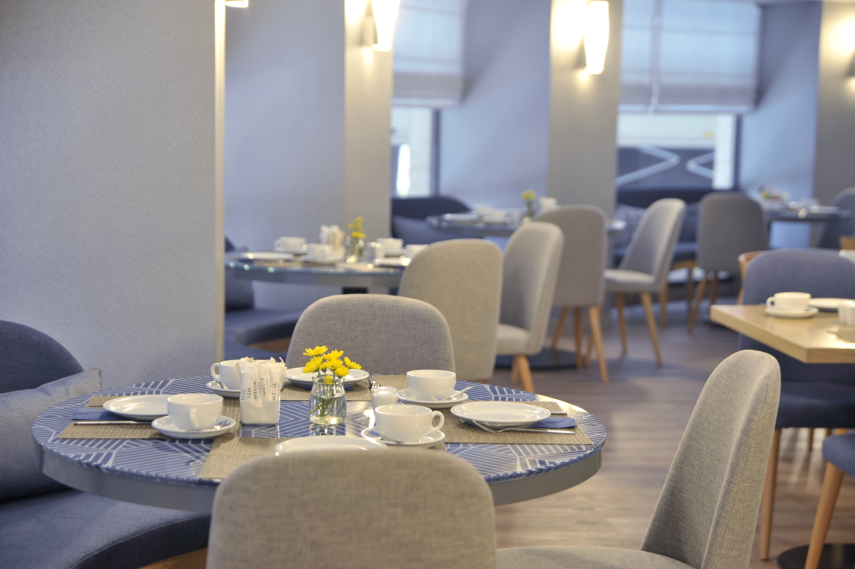 Modern hotel dining room with tables set for breakfast, blue and grey decor.
