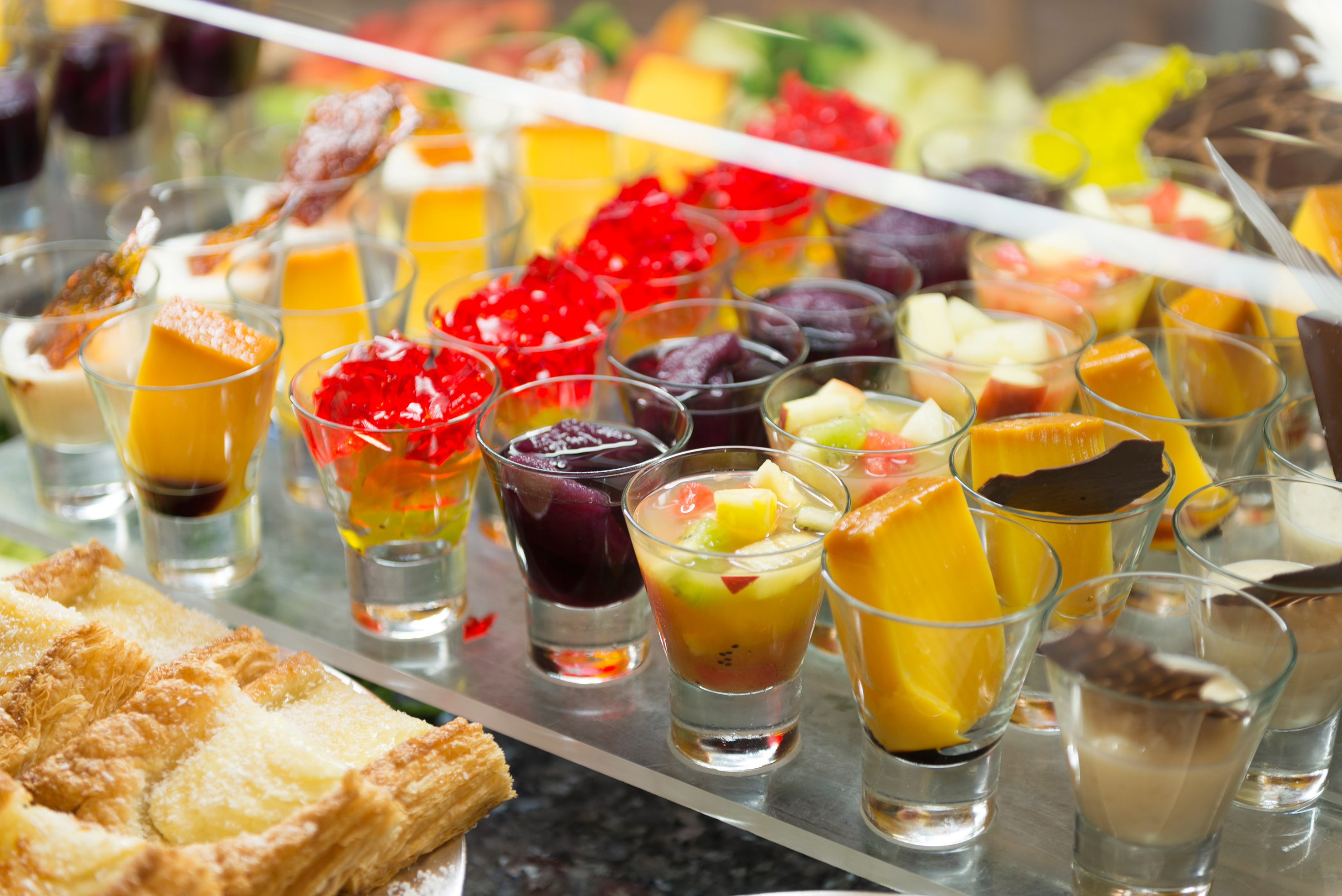 Dessert buffet with colorful mini puddings, jellies, fruit salad, pastries.