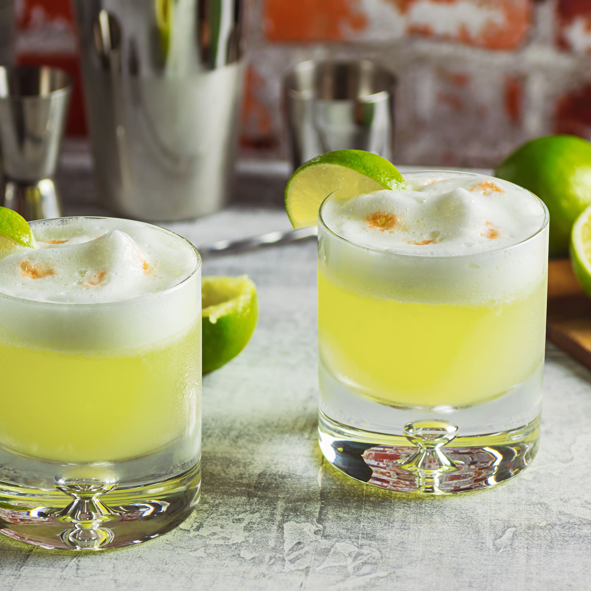 two glasses of yellow liquid with limes and a cutting board