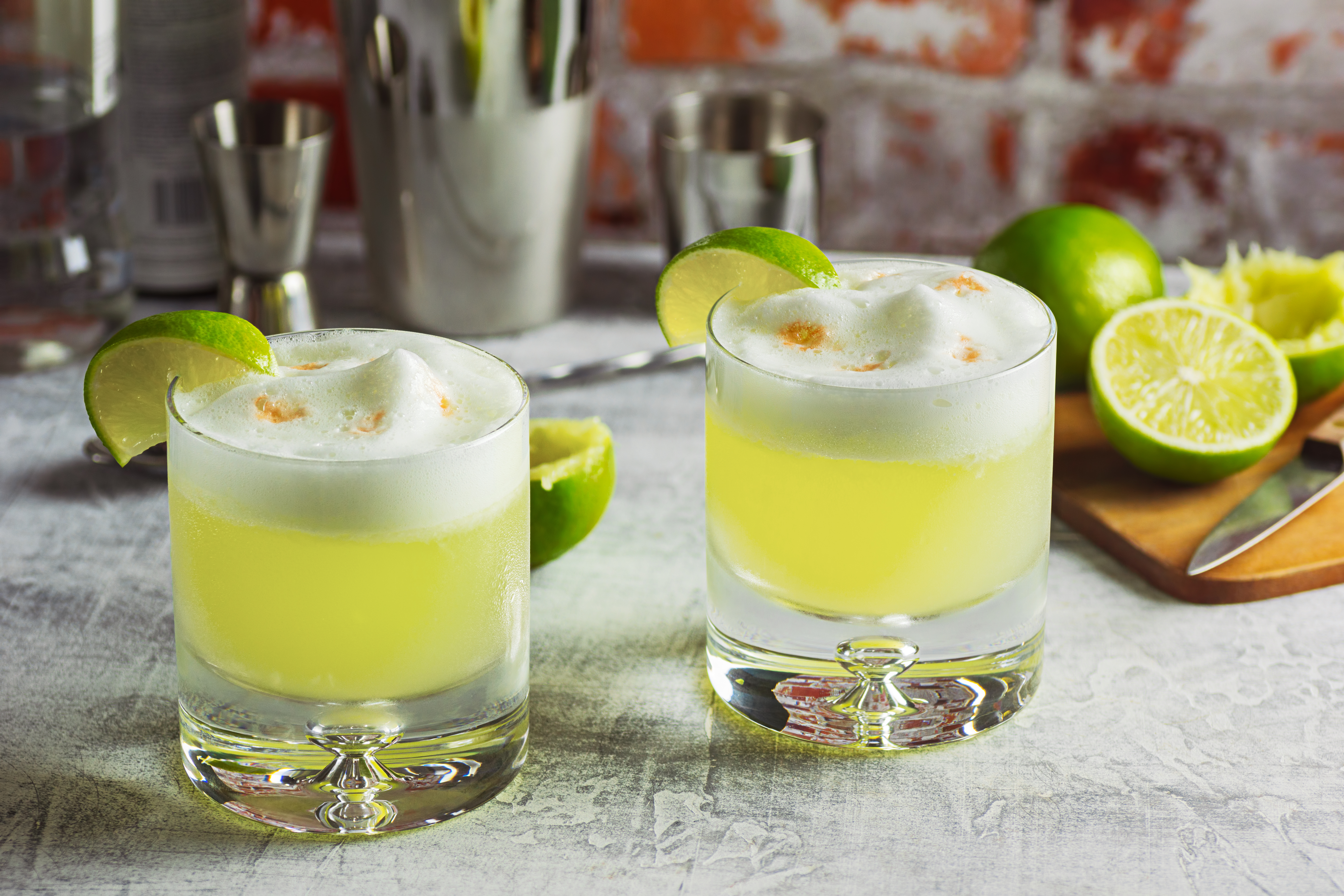 two glasses of yellow liquid with limes and a cutting board