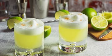 two glasses of yellow liquid with limes and a cutting board