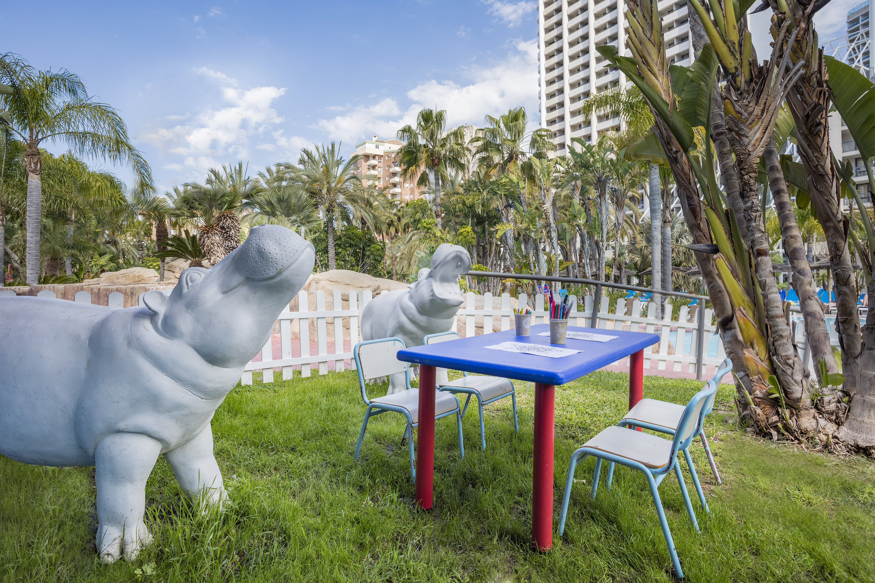 White hippo statues, children's coloring table, tropical resort with palm trees.