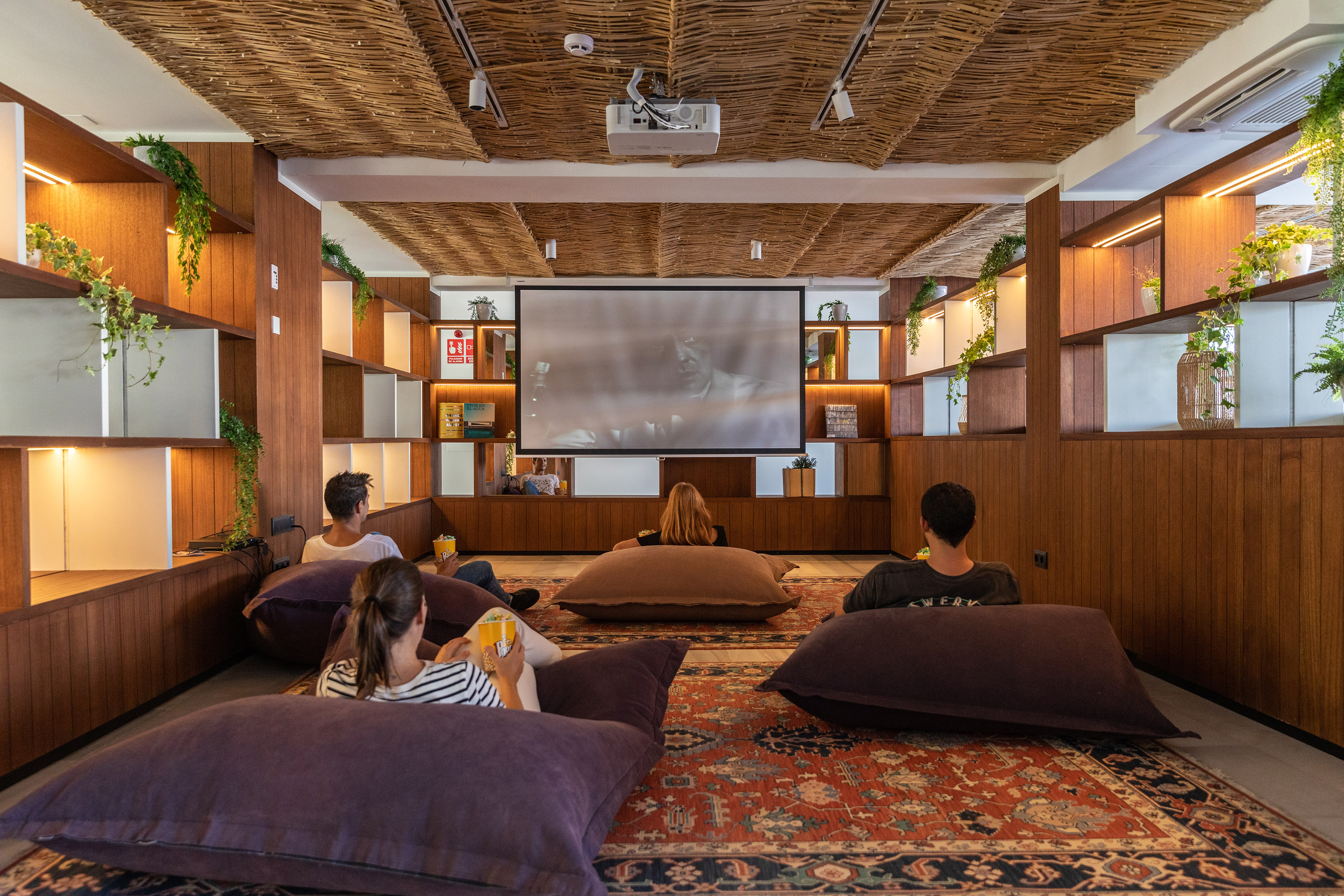 Cozy cinema lounge with people on bean bags watching film on projector.