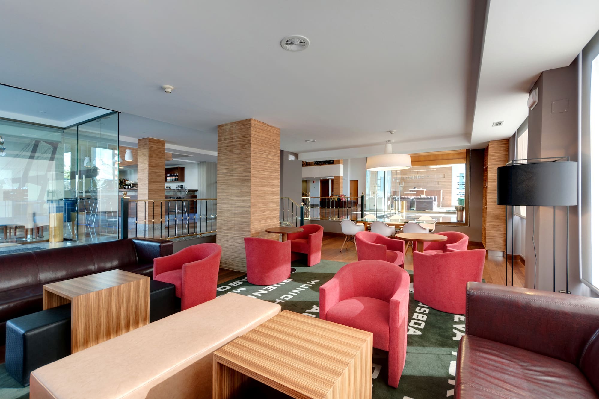 Modern hotel lounge with red armchairs, leather sofas, and a patterned rug.