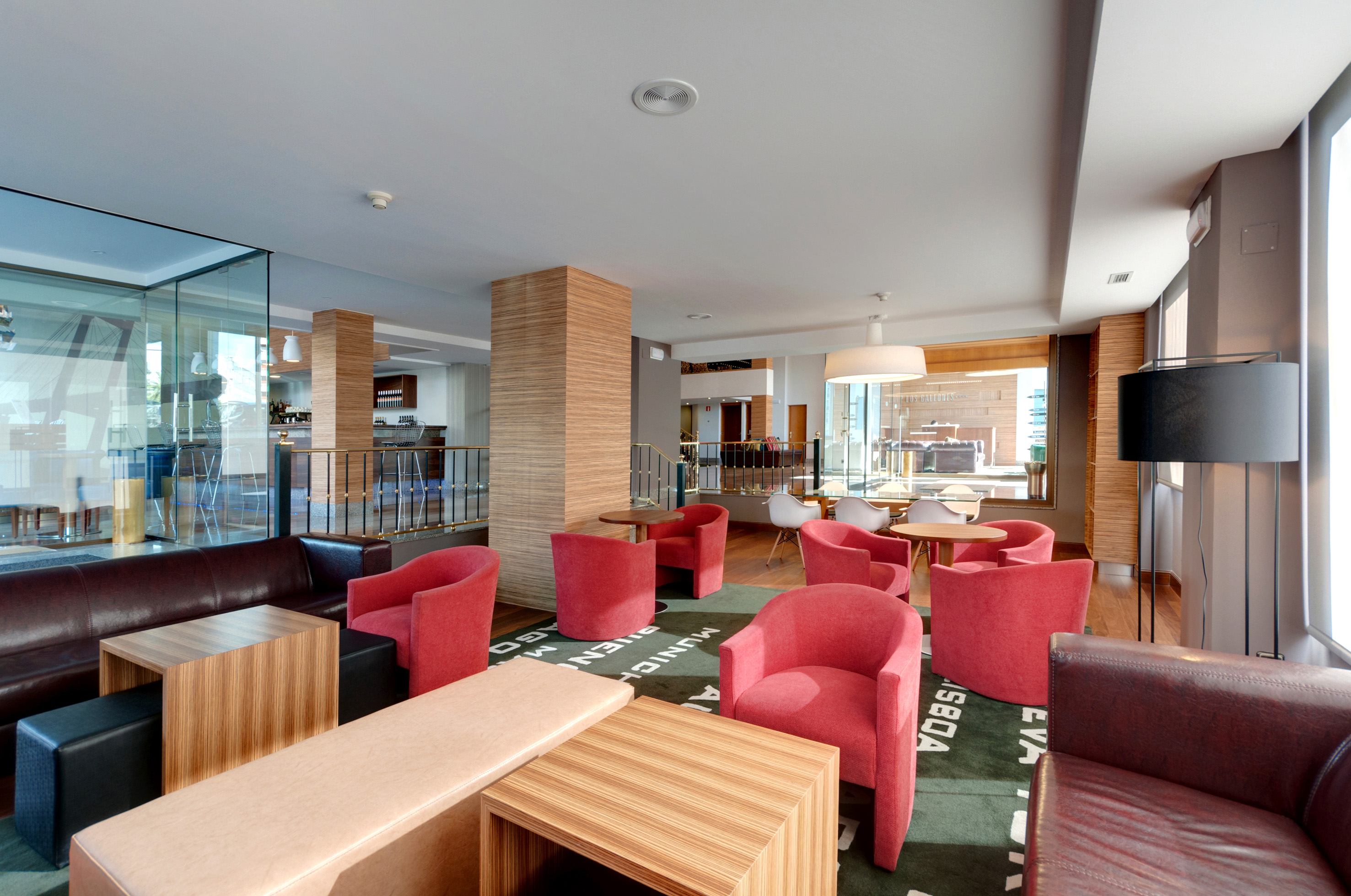 Modern hotel lounge with red armchairs, leather sofas, and a patterned rug.
