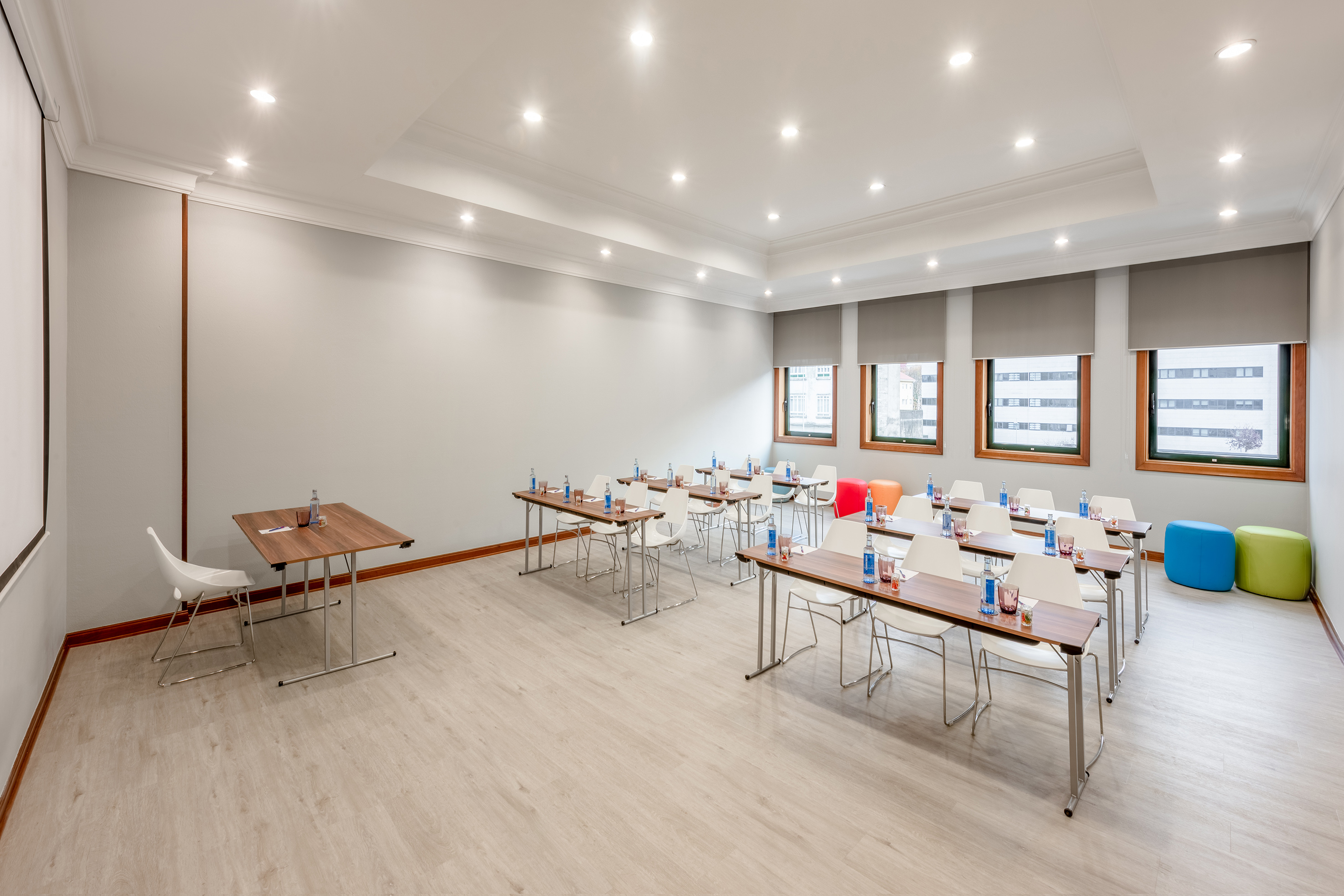Modern conference room with tables, white chairs, projection screen, and windows.