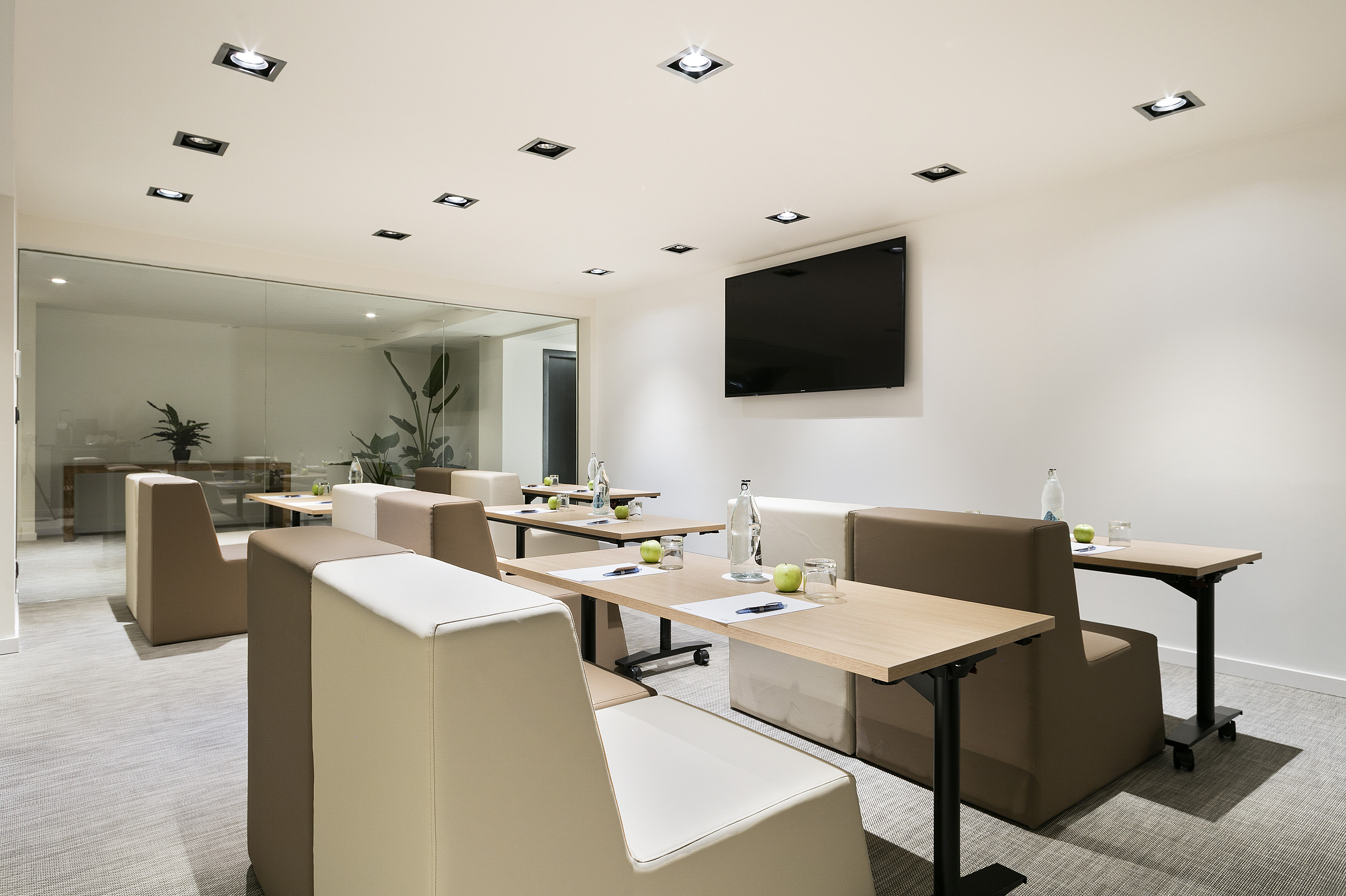 Modern conference room with neutral seating, tables, screen, glass partition.