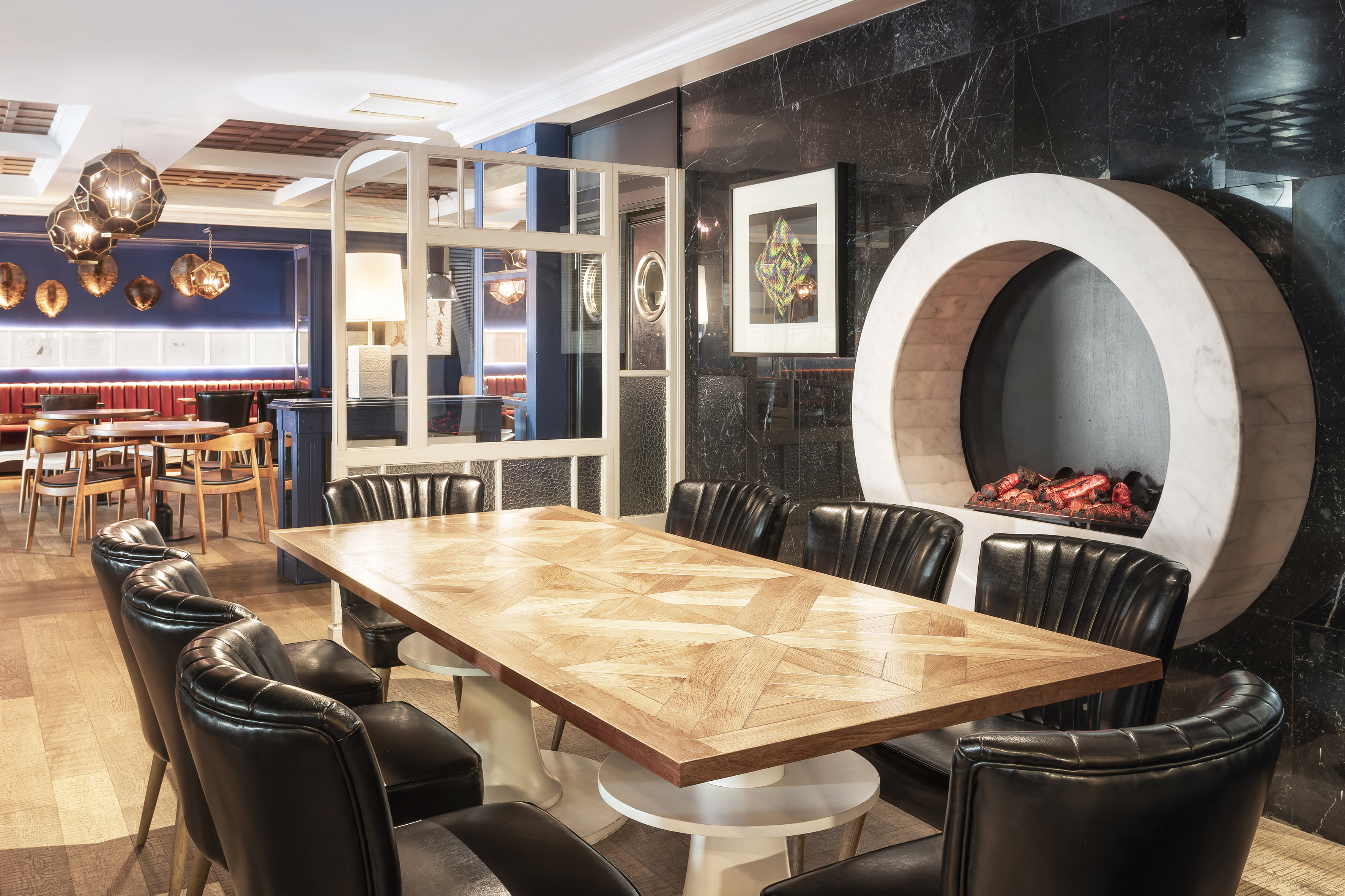 Stylish restaurant dining room: wood table, black chairs, circular marble fireplace.