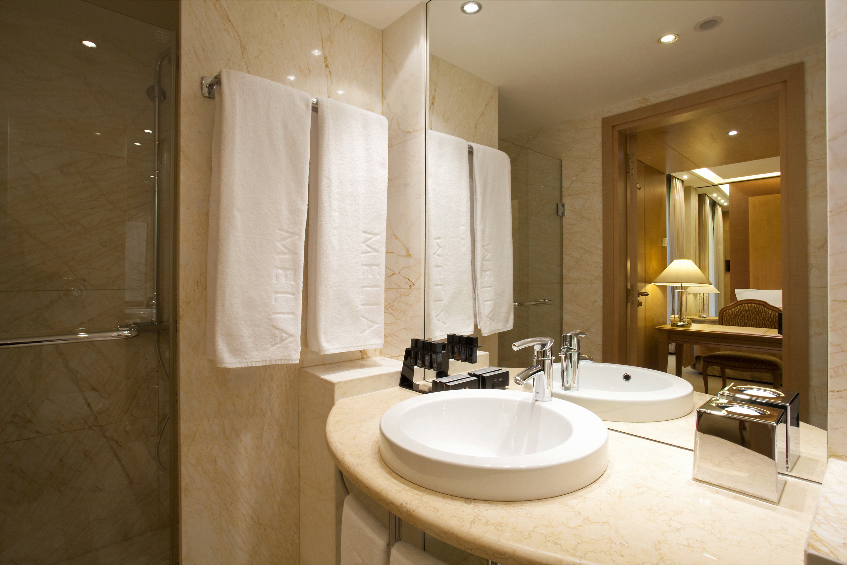 Elegant hotel bathroom with marble vanity, white sink, Meliá towels, and glass shower.
