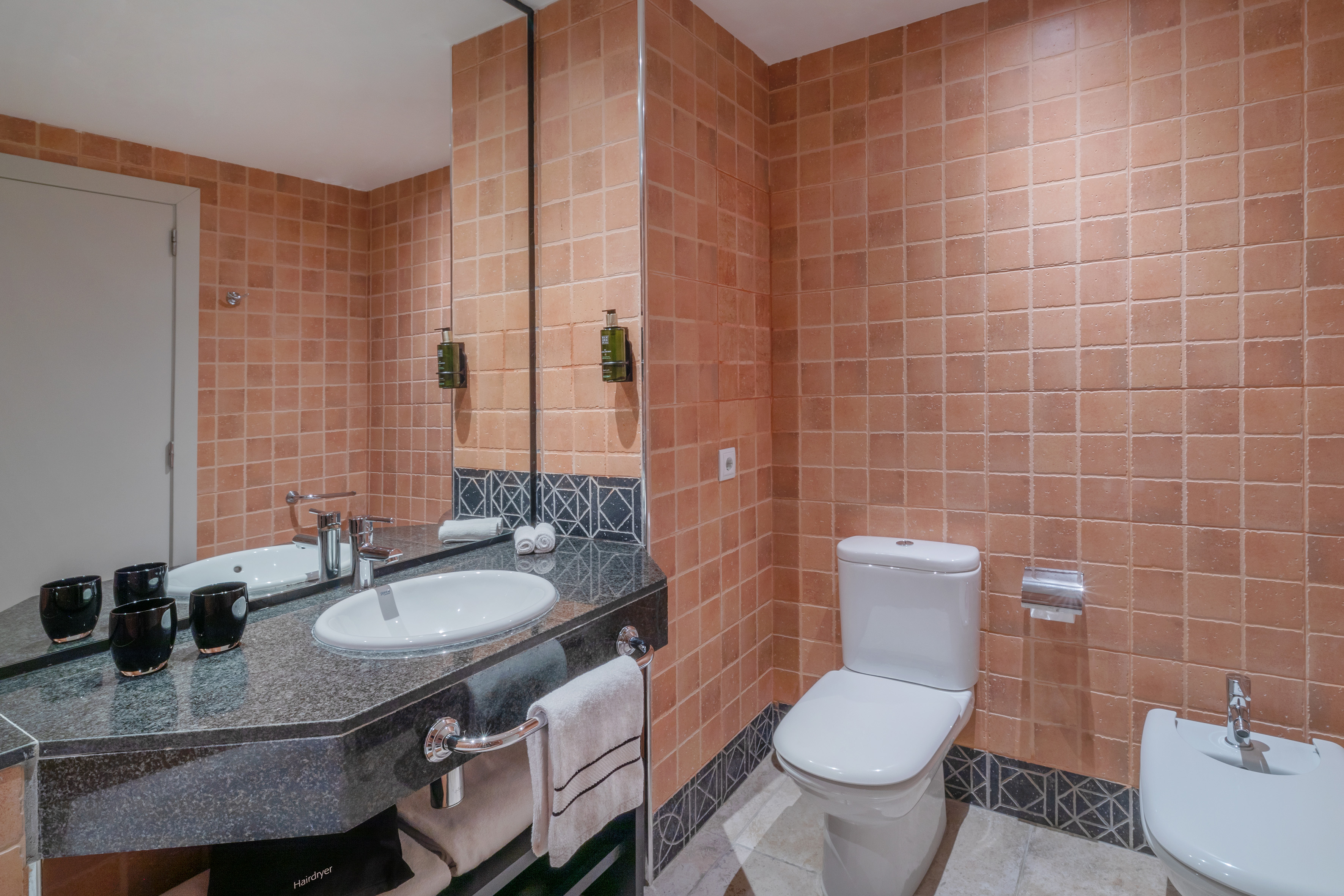 Hotel bathroom with terracotta tile, single sink, toilet, and bidet.