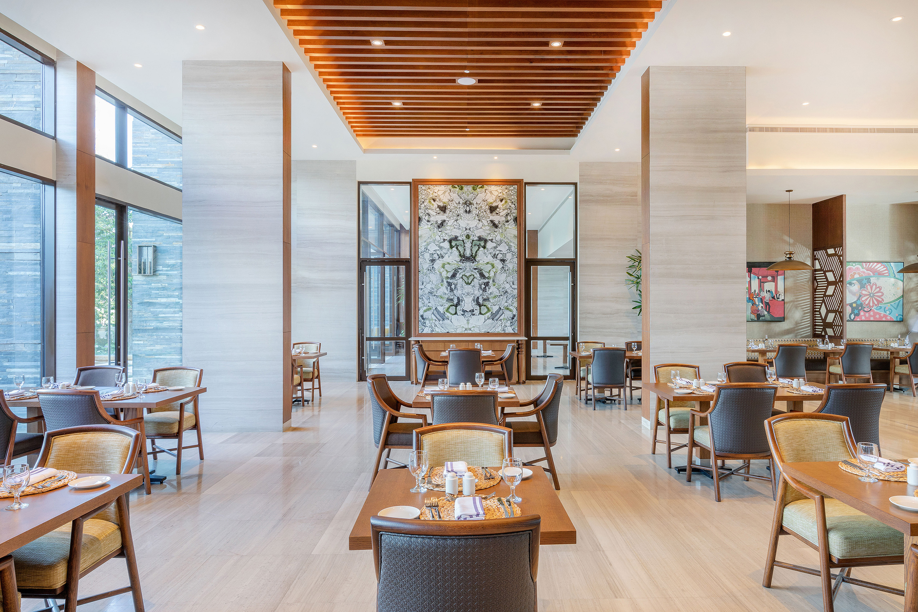 Modern restaurant dining room with wooden tables, elegant chairs, and large windows.