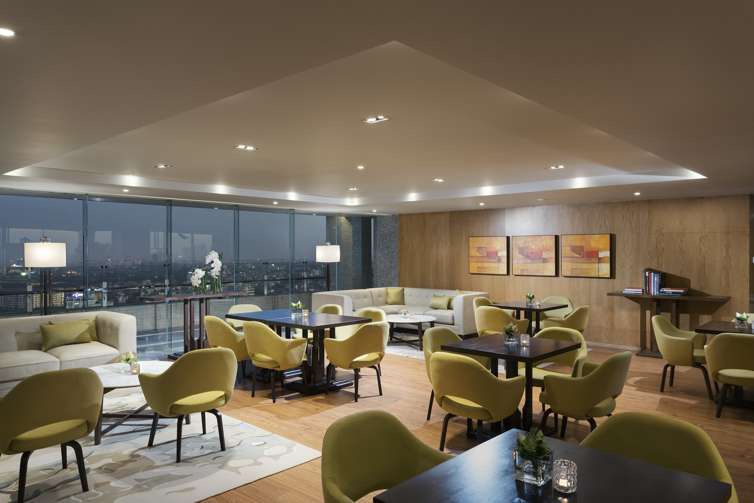 Elegant lounge with city view, modern green chairs, and ambient lighting.