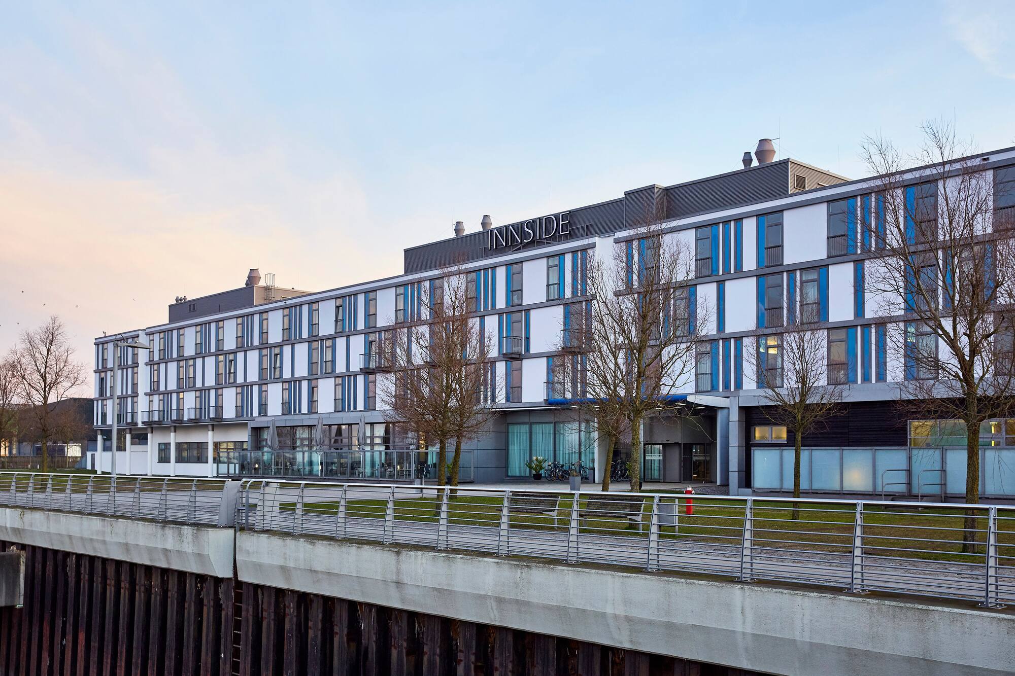 Modern INNSIDE hotel building, white and blue, along a waterfront.
