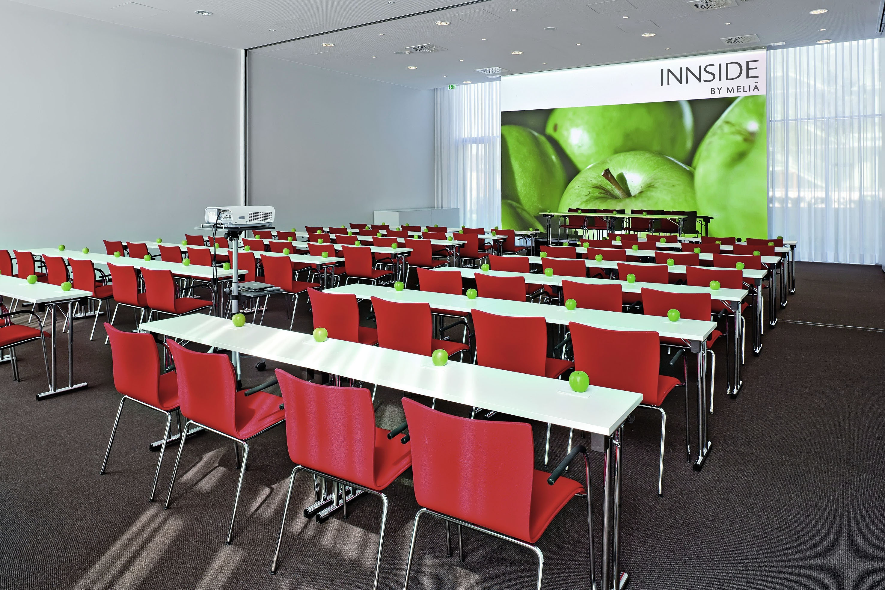 INNSIDE by Meliá conference room with red chairs, tables, and green apples.