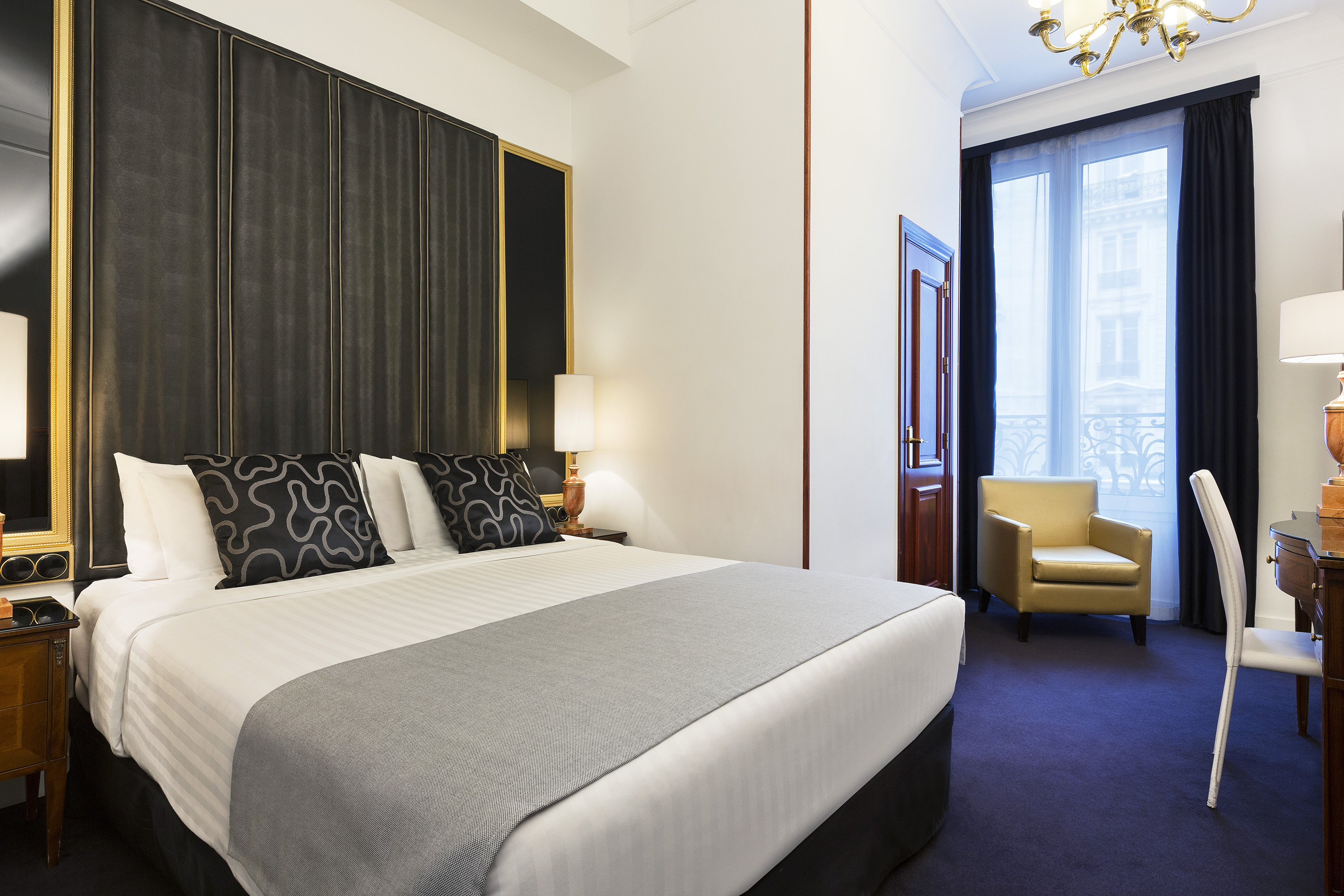 Elegant hotel room with bed, dark paneled headboard, and gold armchair.