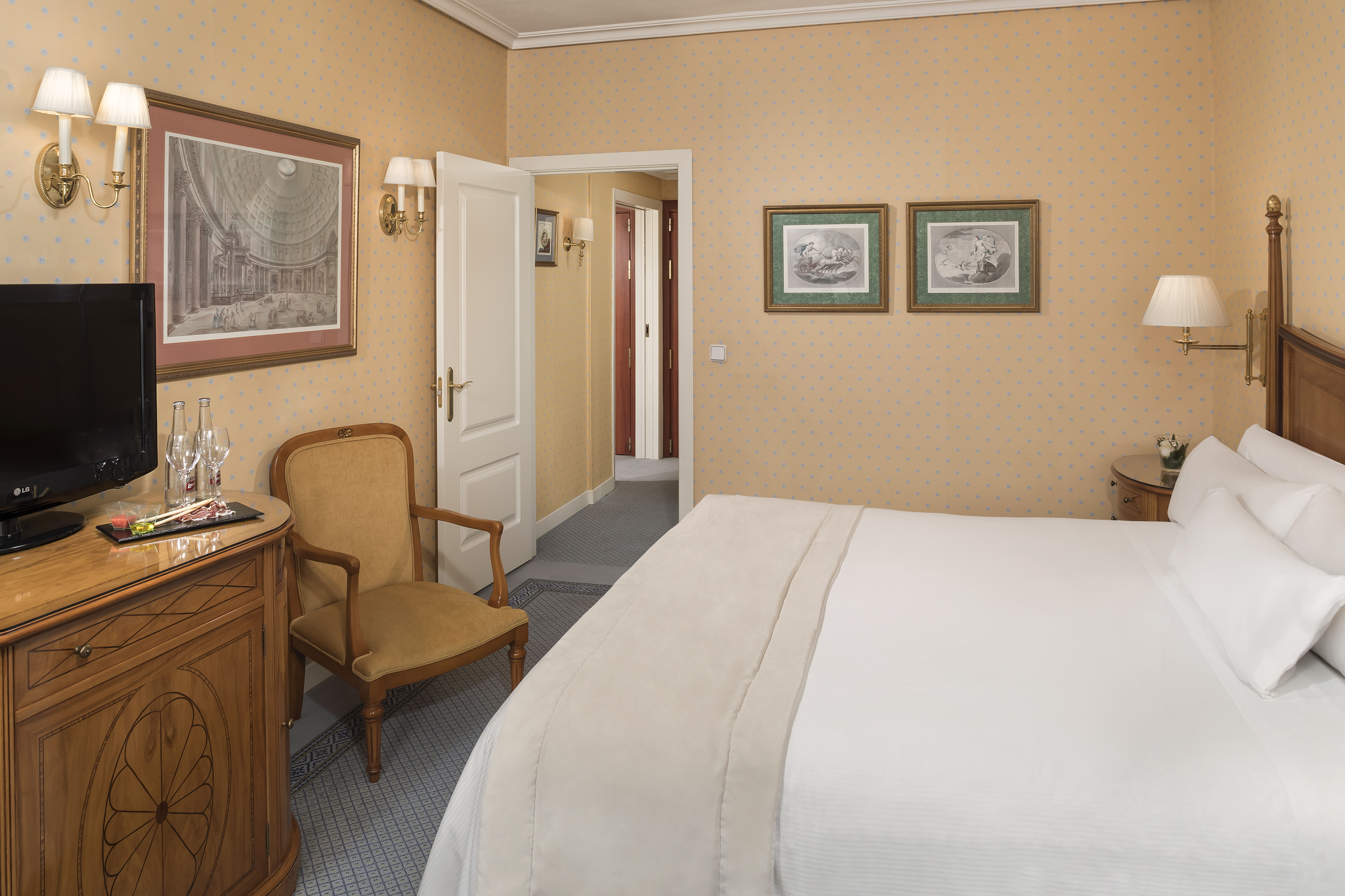 Hotel room with bed, yellow patterned walls, classic wood furniture, and framed art.