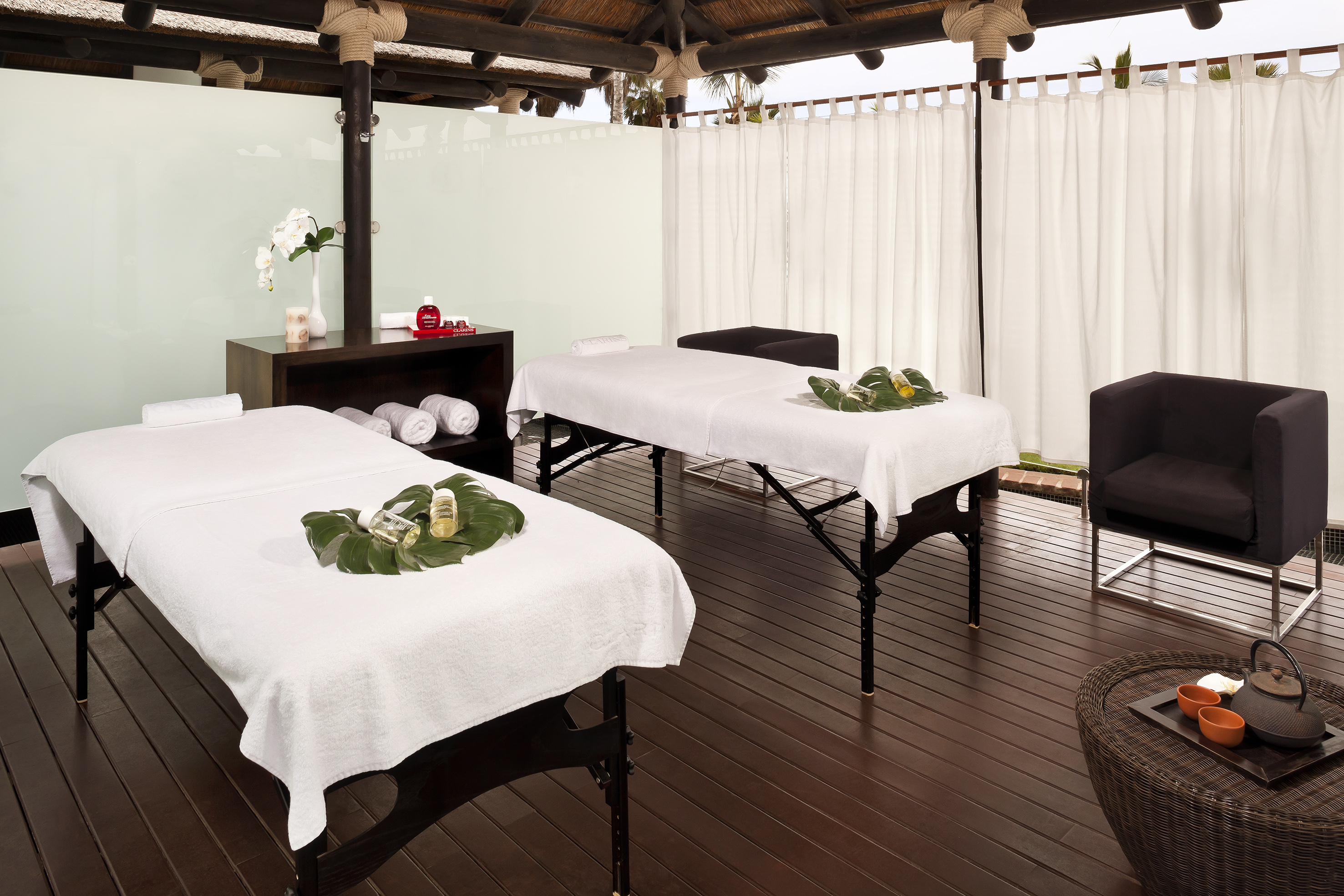 Tropical luxury spa room with two massage tables and dark wood floor.