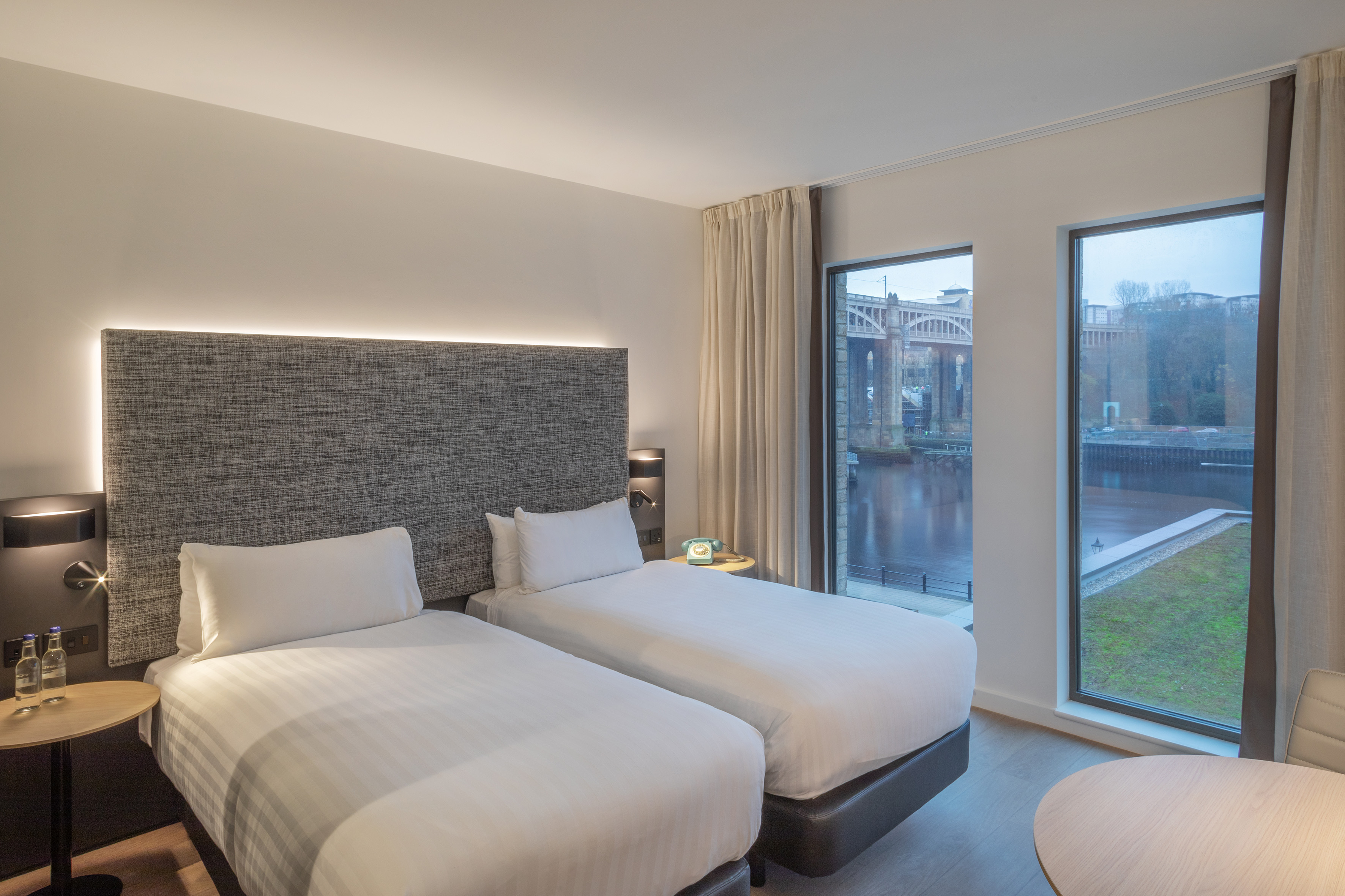 Modern hotel room with twin beds, river view, and bridge cityscape.