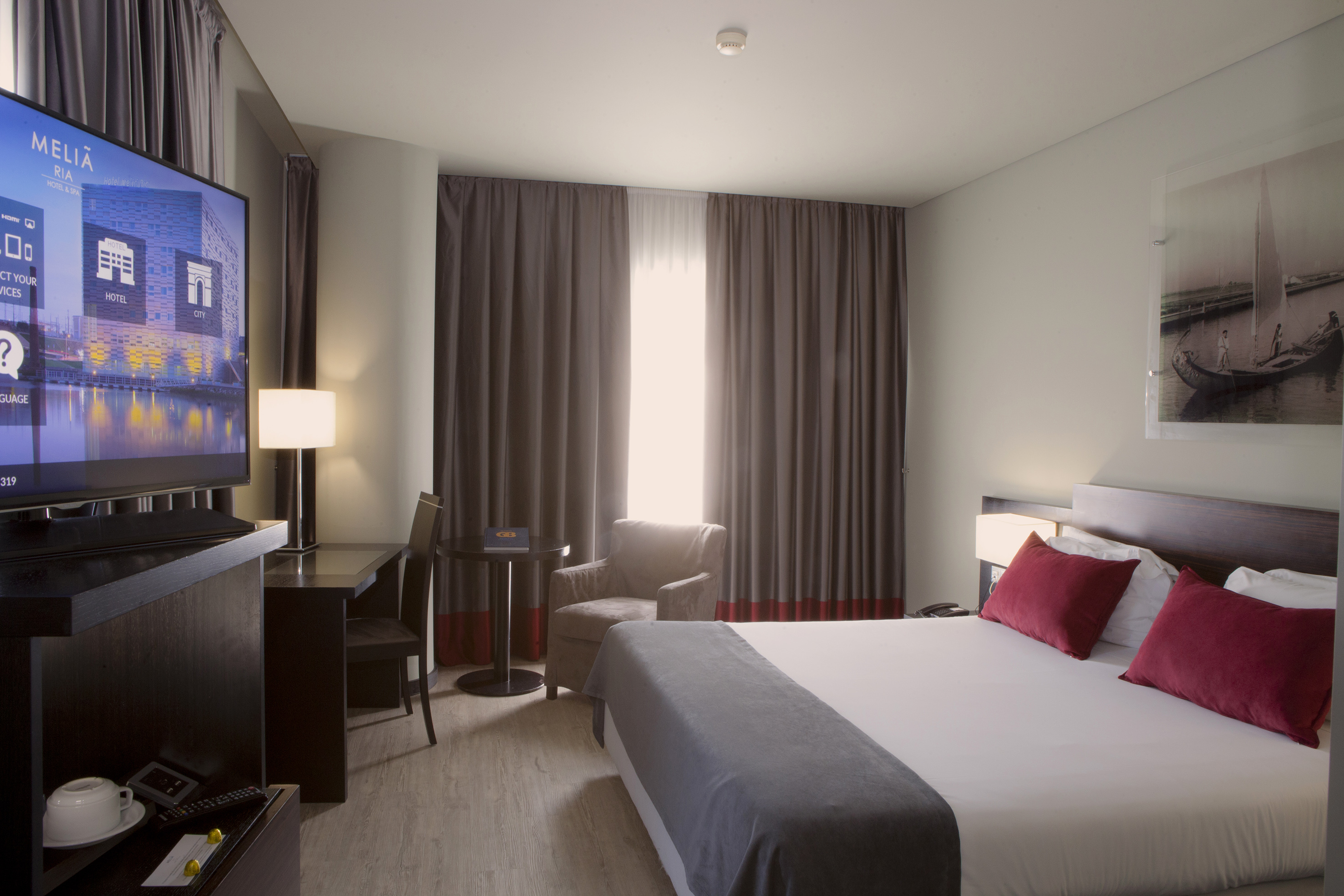 Meliã Ria hotel room with bed, large TV, desk, and comfortable armchair.