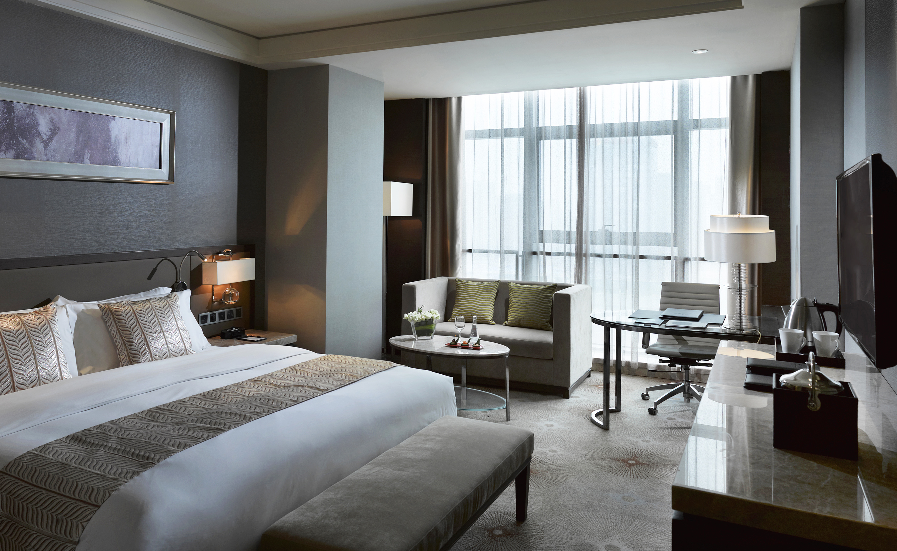Modern hotel suite featuring a king bed, sofa, and dedicated workspace.